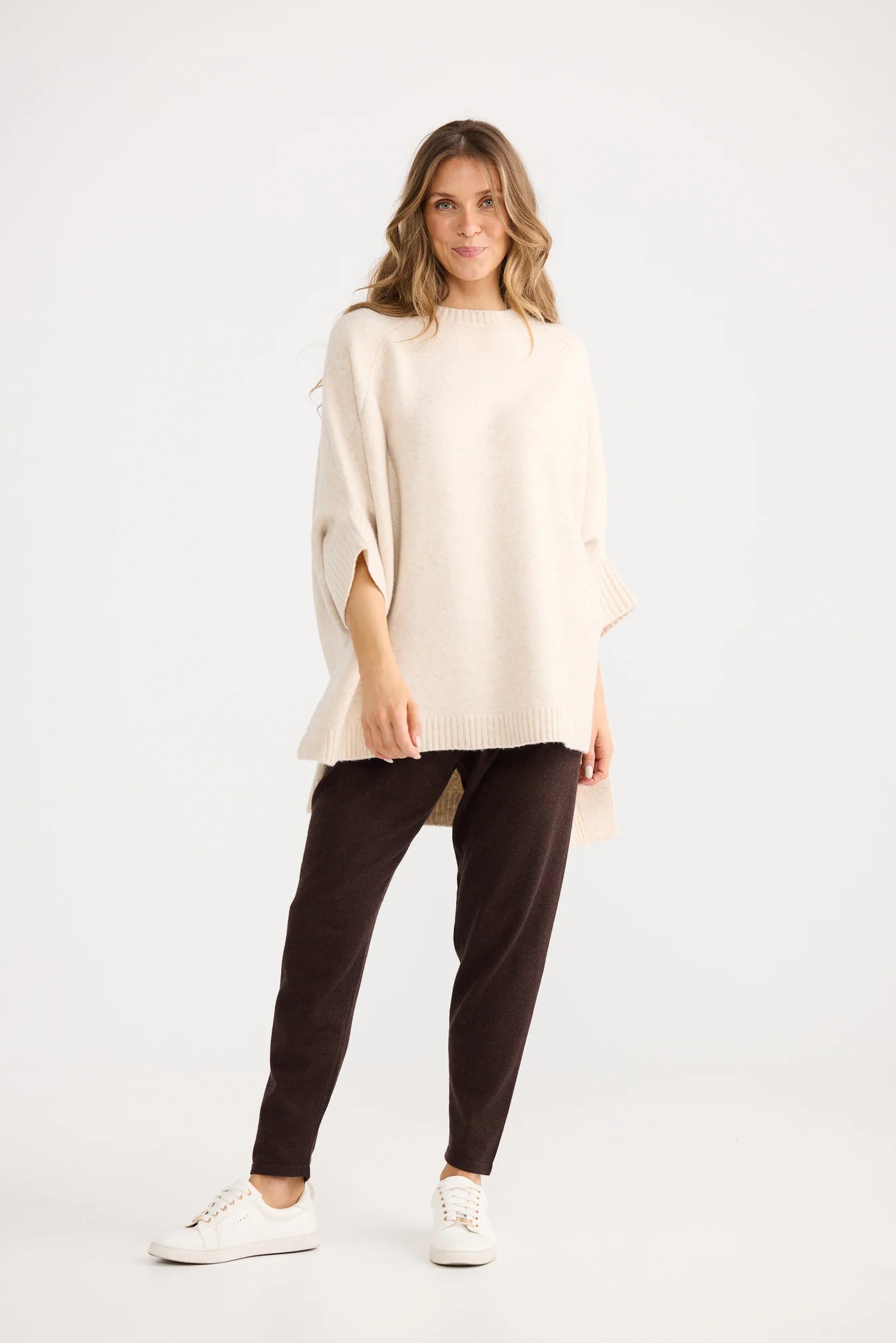 Woman wearing a Home Love cream poncho and black pants on a white background