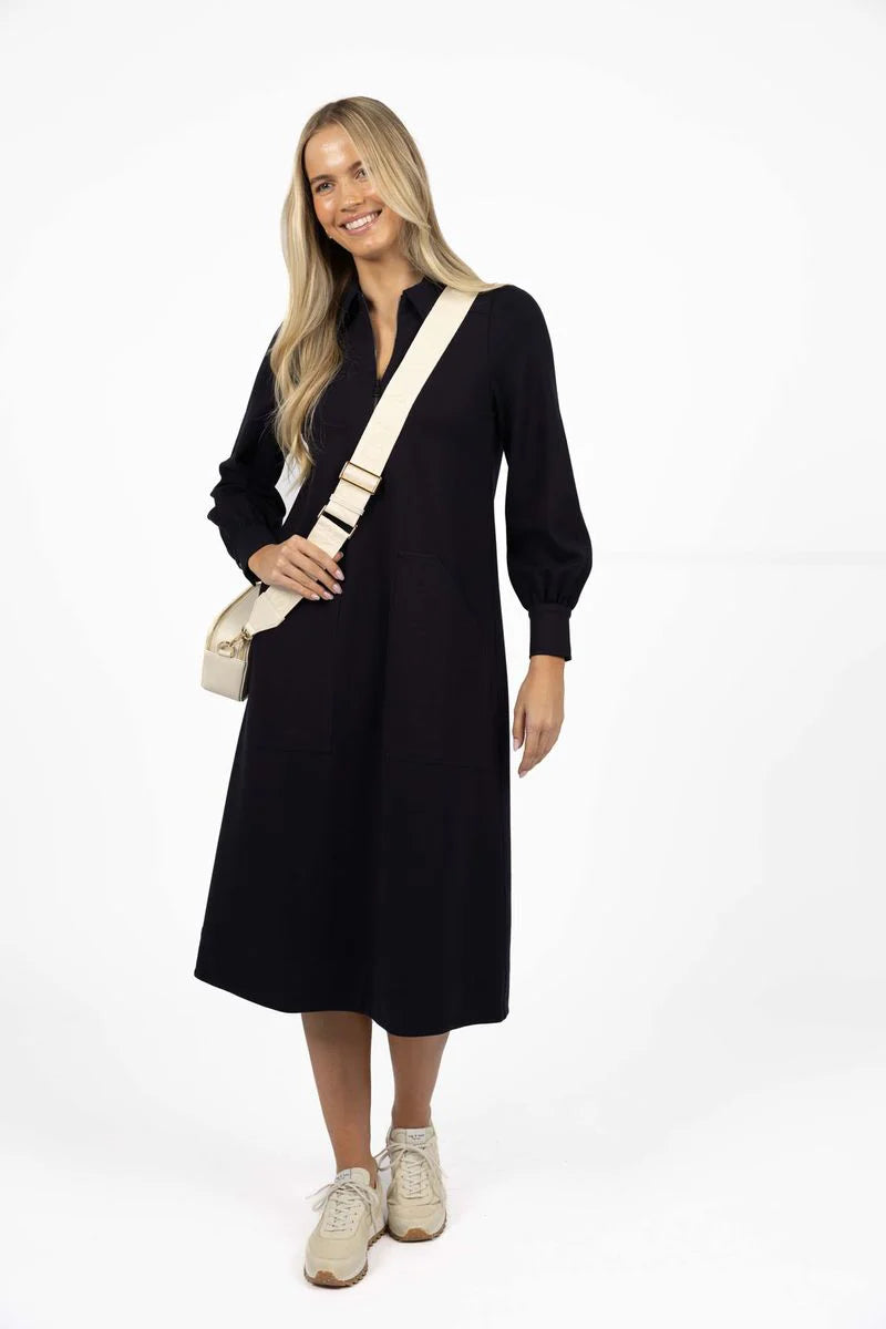 Woman wearing a Humidity black dress with a beige bag on a white background