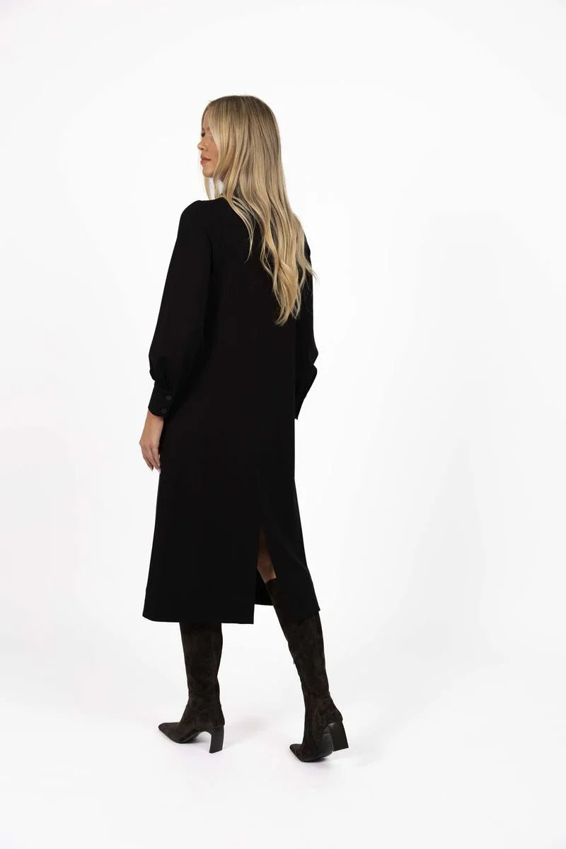 Woman wearing a Humidity long black dress with a slit on a white background