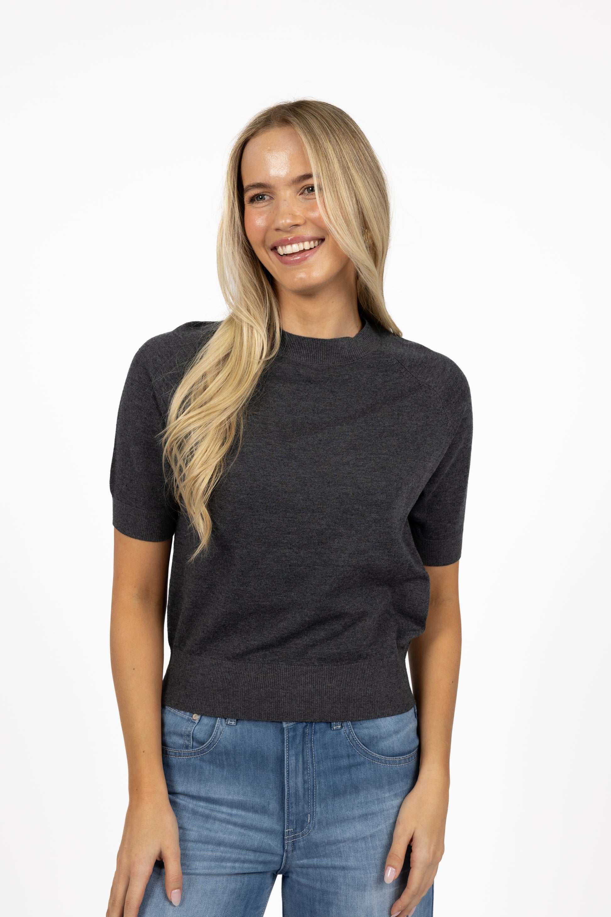 Woman wearing a Humidity dark gray sweater and blue jeans on a white background
