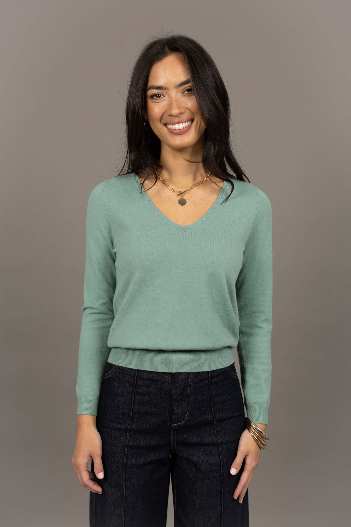 Collection of Woman wearing a Humidity light green sweater and black pants against a gray background in a gallery layout