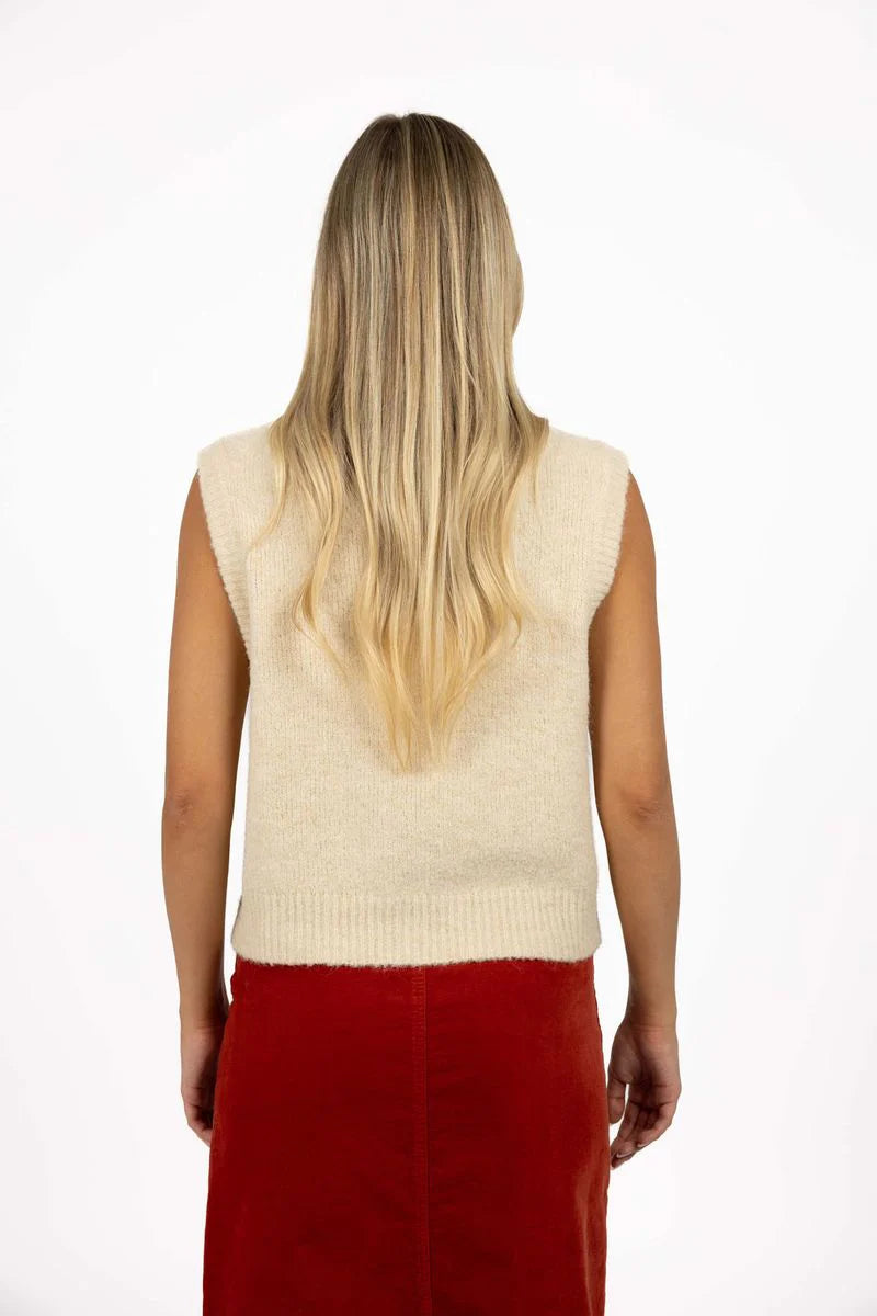 Image of Woman wearing a Humidity beige sleeveless sweater over a red skirt on a white background