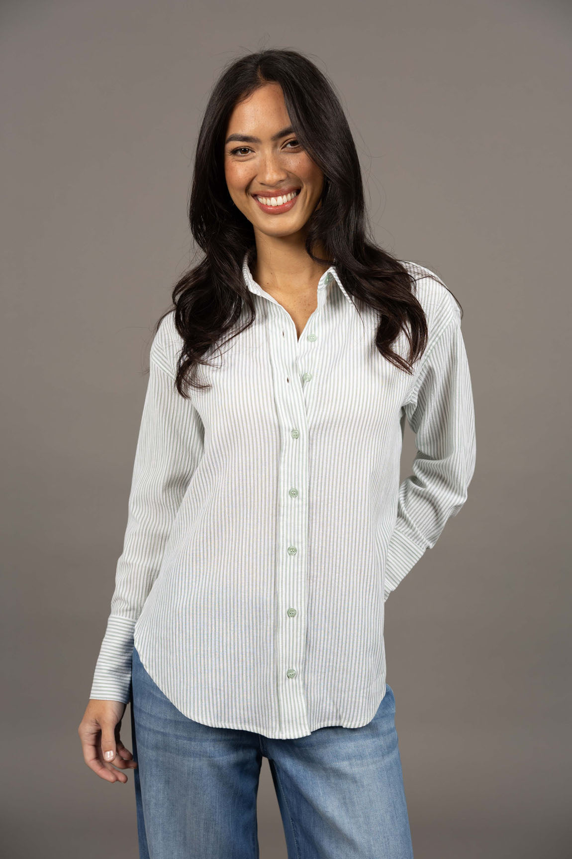 Woman wearing a Humidity green button-up shirt with blue jeans against a gray background