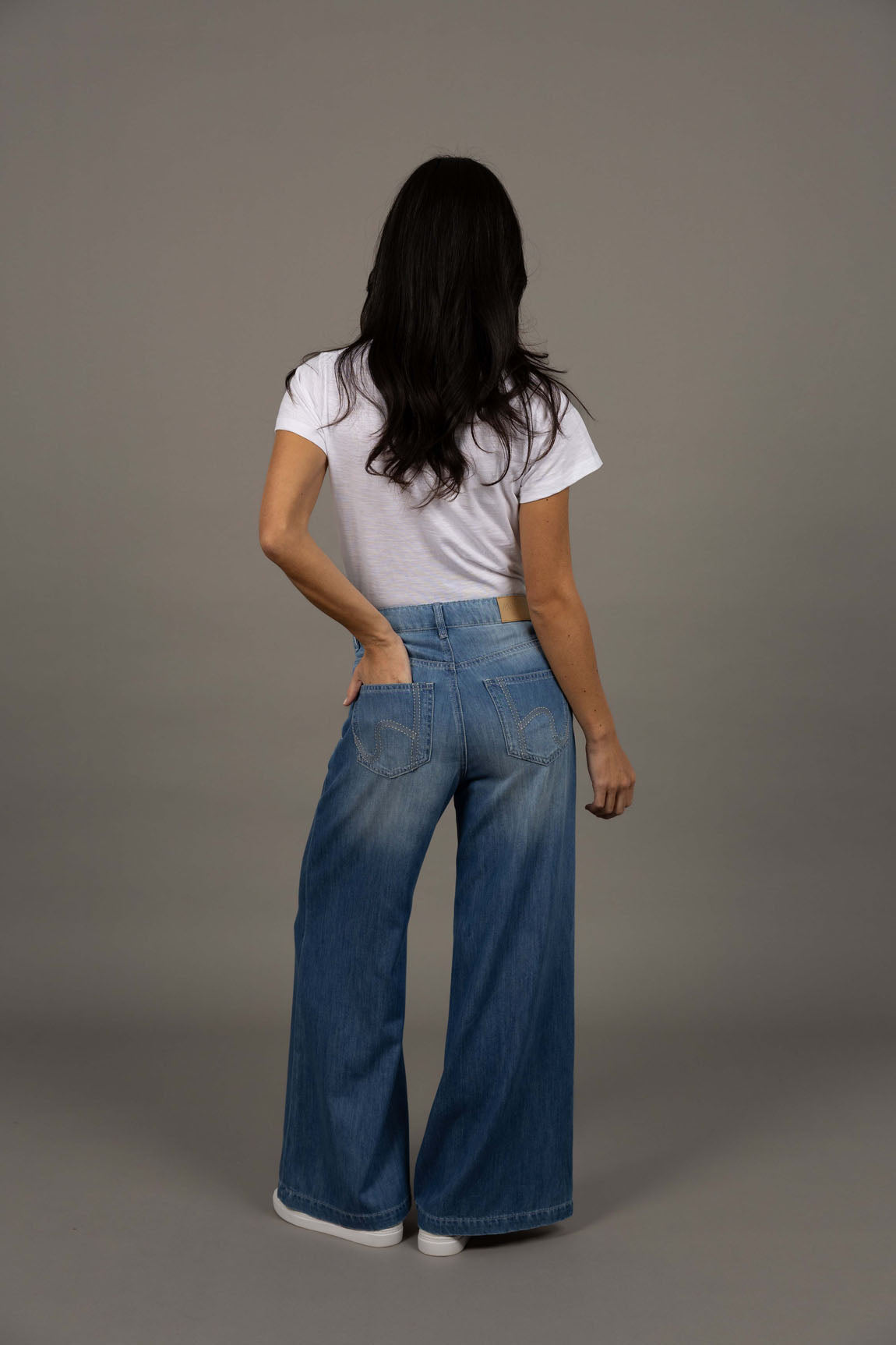 Woman wearing a white t-shirt and Humidity blue jeans against a gray background