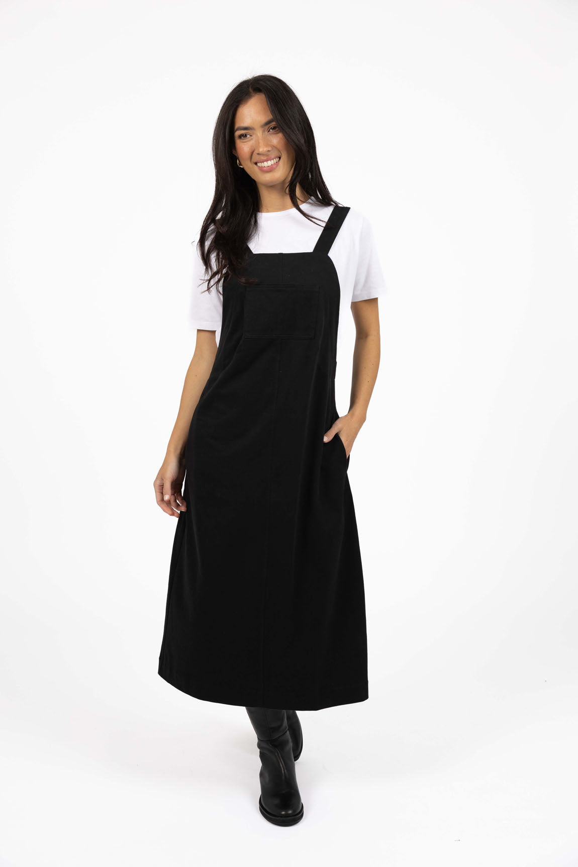 Image of Woman wearing a Humidity black pinafore dress over a white shirt on a white background