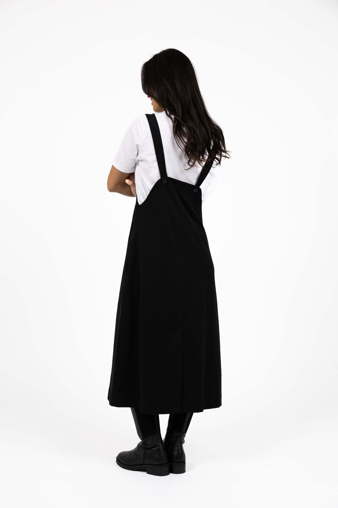 Image of Person wearing a Humidity black pinafore dress over a white shirt on a white background