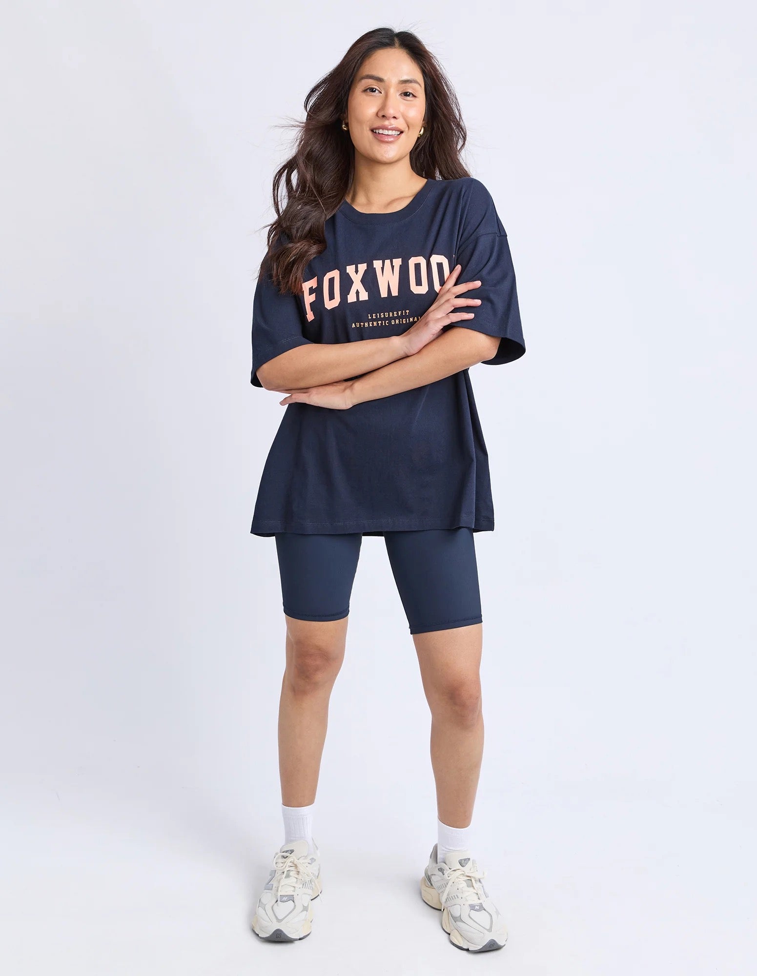 Woman wearing a Foxwood navy blue t-shirt with 'FOXWOOD' branding in peach and matching shorts on a white background