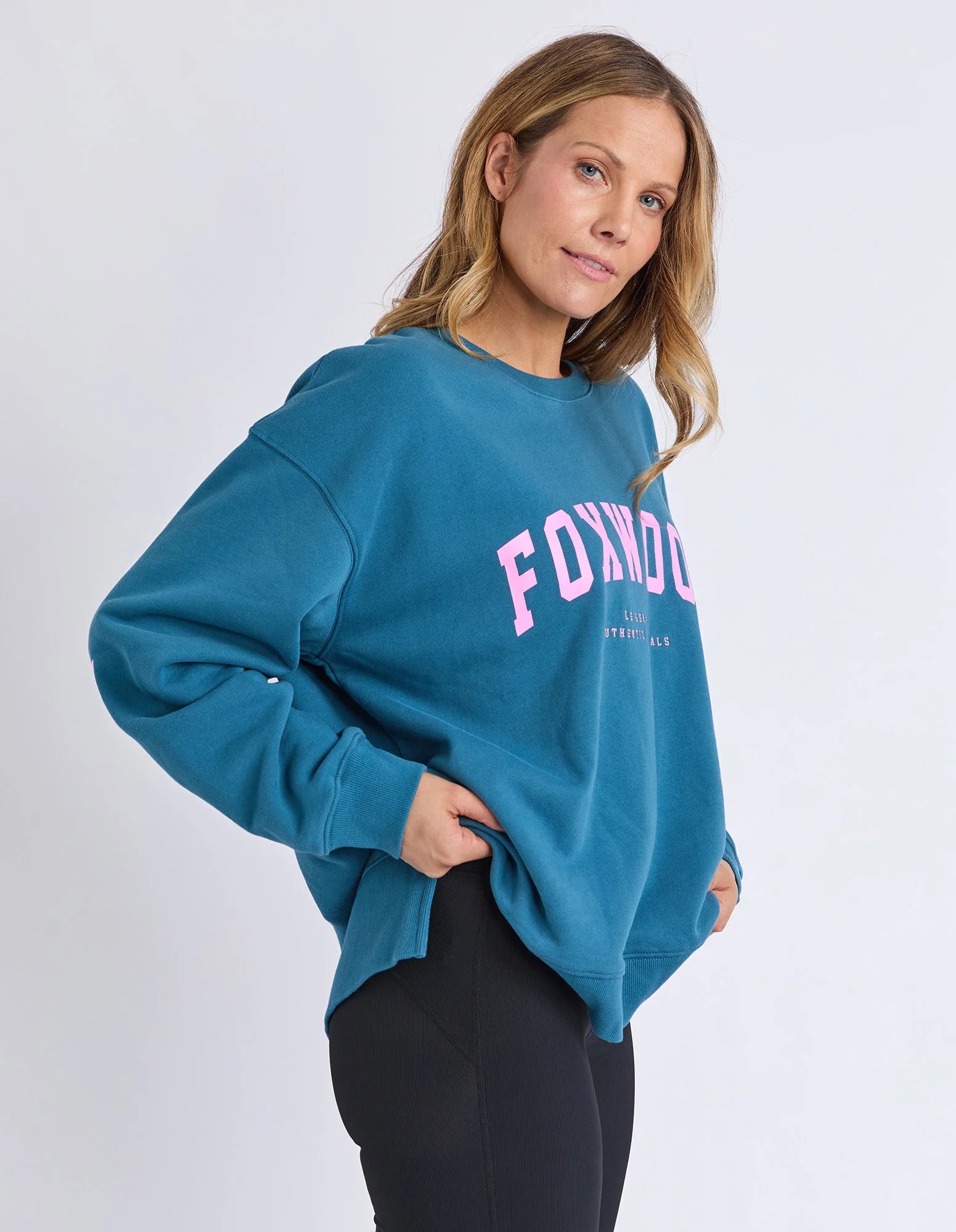 Woman wearing a blue Foxwood jumper with pink text on a white background