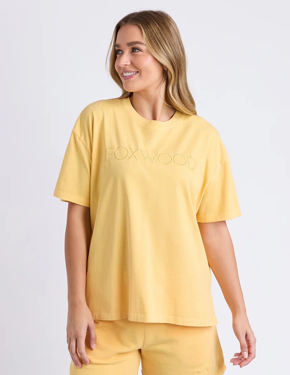 Woman wearing a yellow t-shirt with 'FOXWOOD' branding on a light grey background
