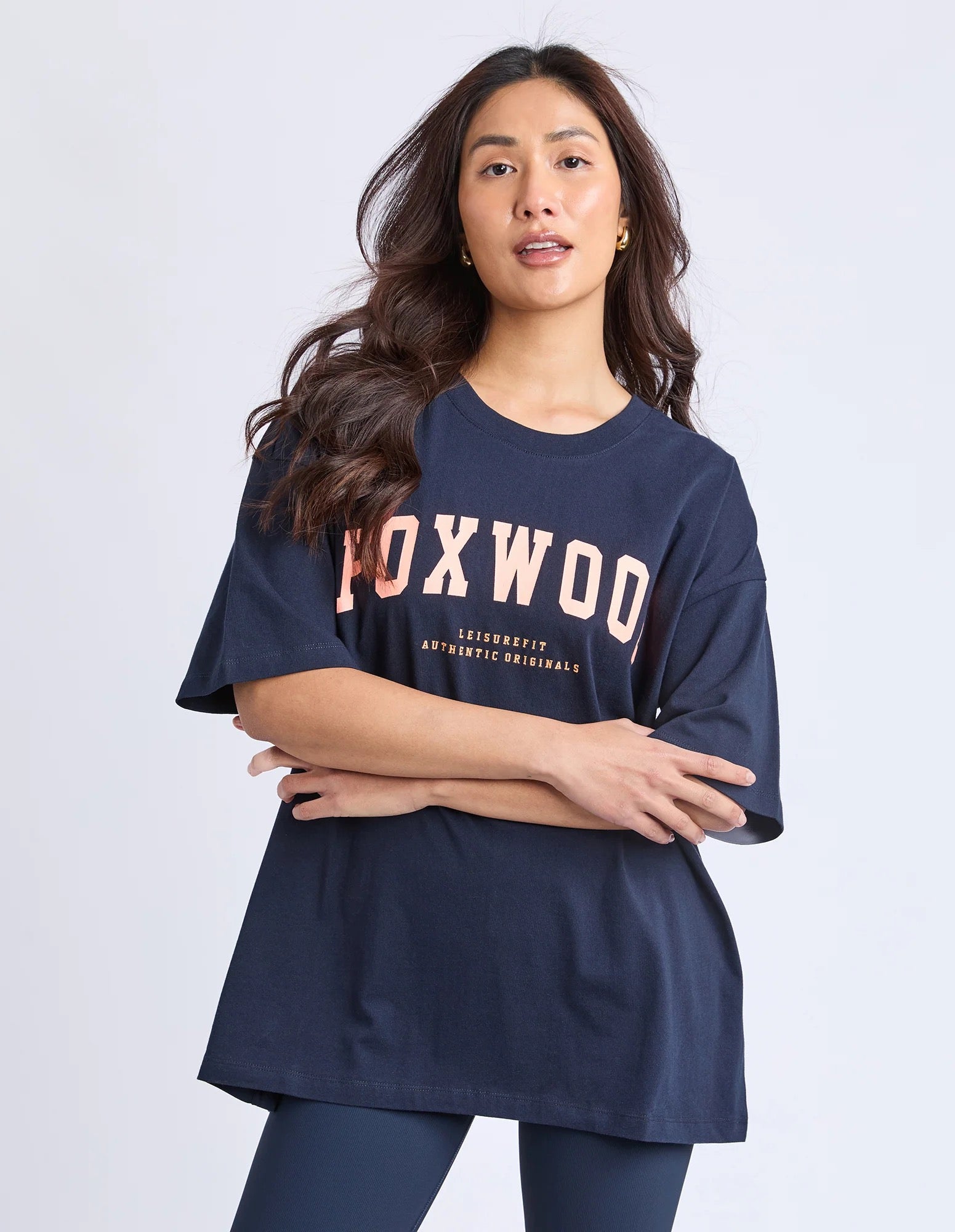 Image of Woman wearing a Foxwood navy blue t-shirt with 'FOXWOOD' printed on it in peaach against a white background