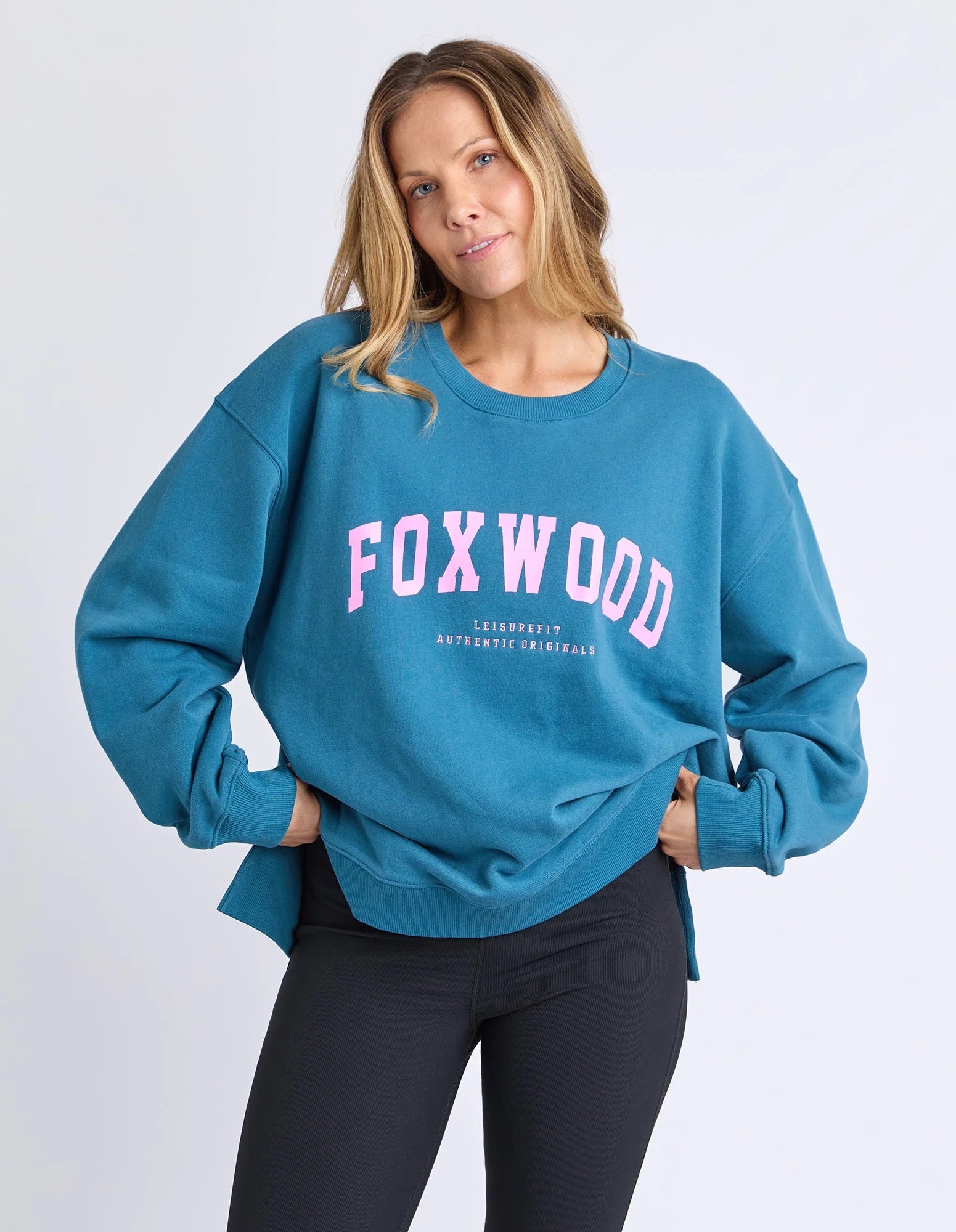 Woman wearing a blue jumper with 'FOXWOOD' printed on it in pink against a white background