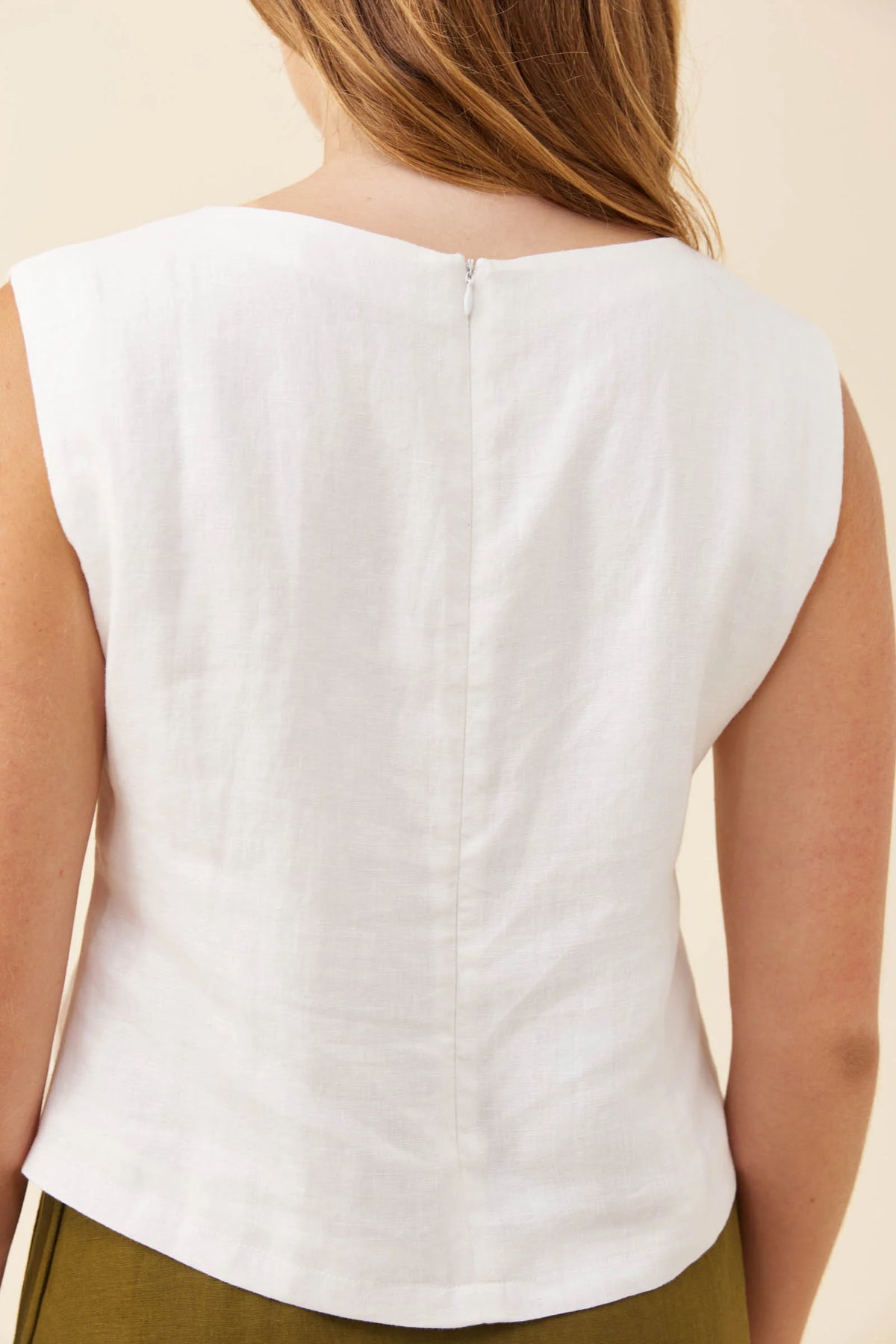 Back view of a Isle of Mine sleeveless white top worn by a model, showing a center back zipper and a curved hem, against a light beige background.