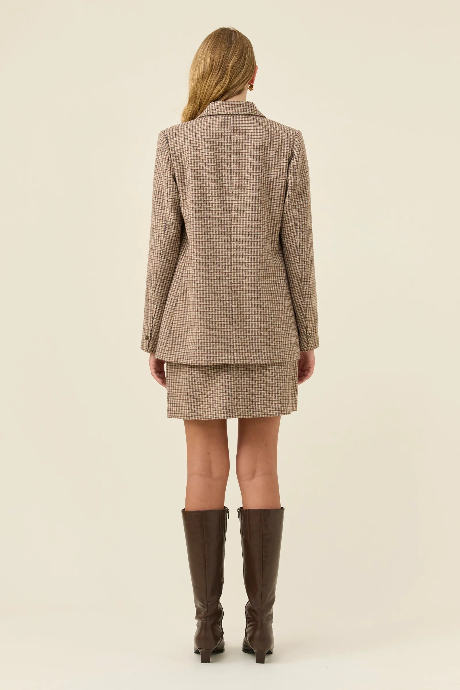 Woman wearing a Isle of Mine beige checkered suit with brown knee-high boots on a beige background