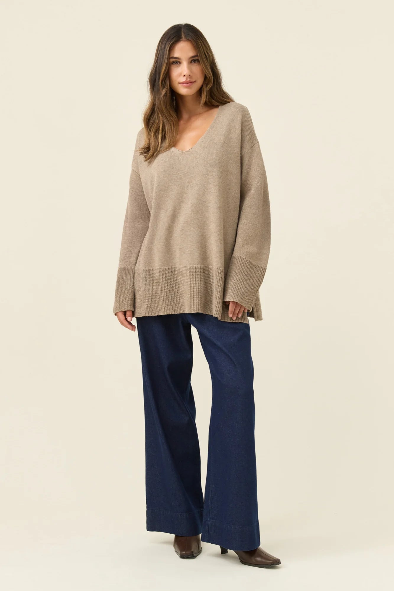 Image of Woman wearing a Isle of Mine beige sweater and blue pants on a plain background