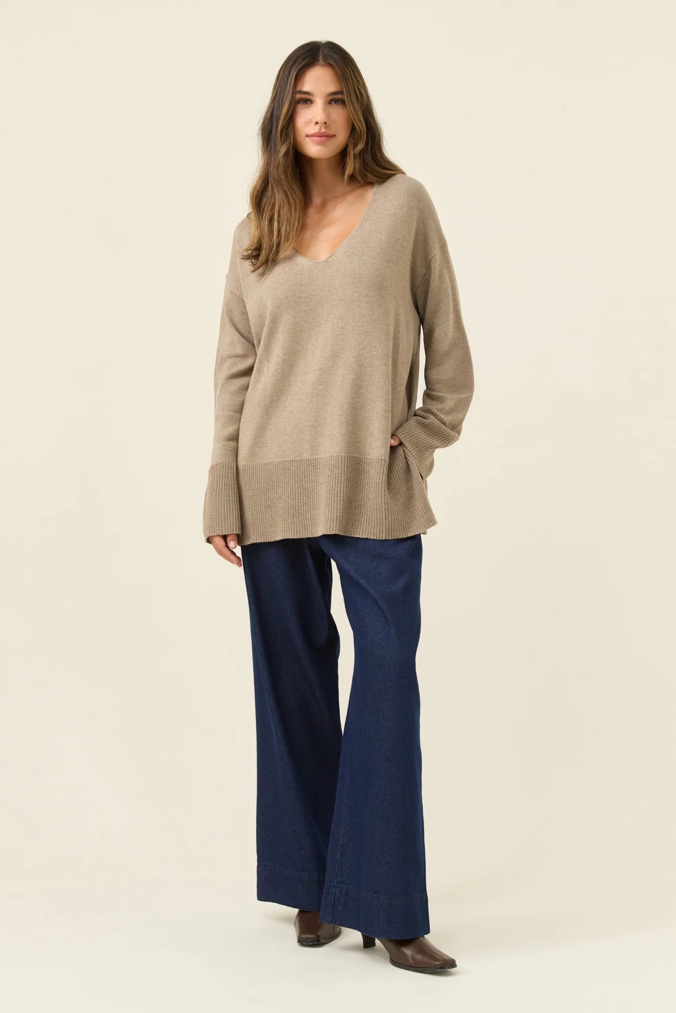 Image of Woman wearing a Isle of Mine beige sweater and blue pants on a plain background