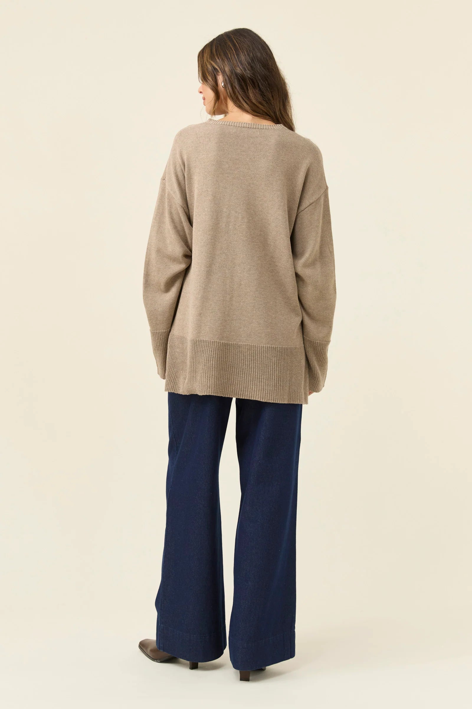 Image of Woman wearing a Isle of Mine beige sweater and blue pants on a beige background