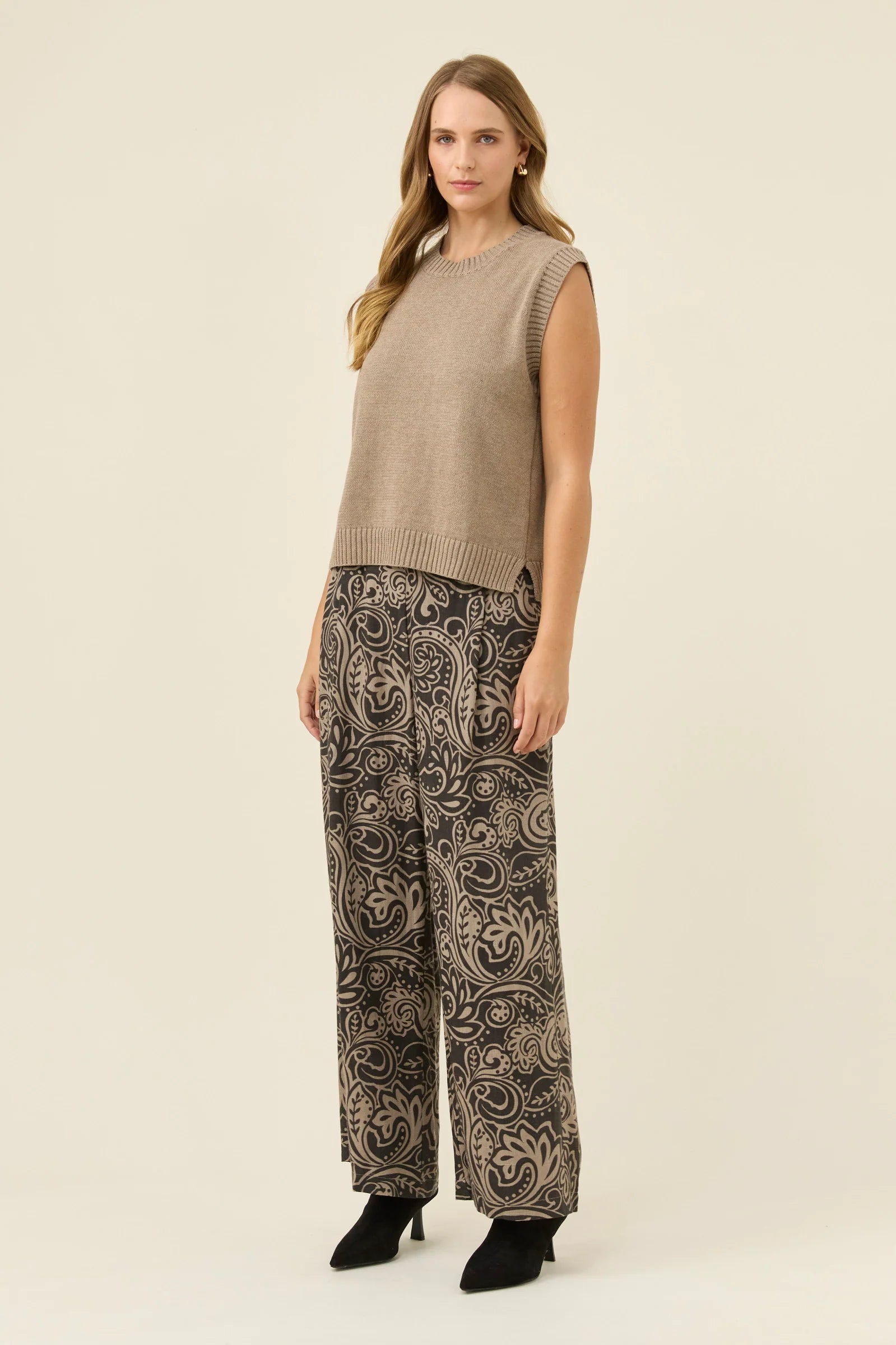 Image of Woman wearing a Isle of Mine beige sleeveless sweater and patterned pants on a beige background