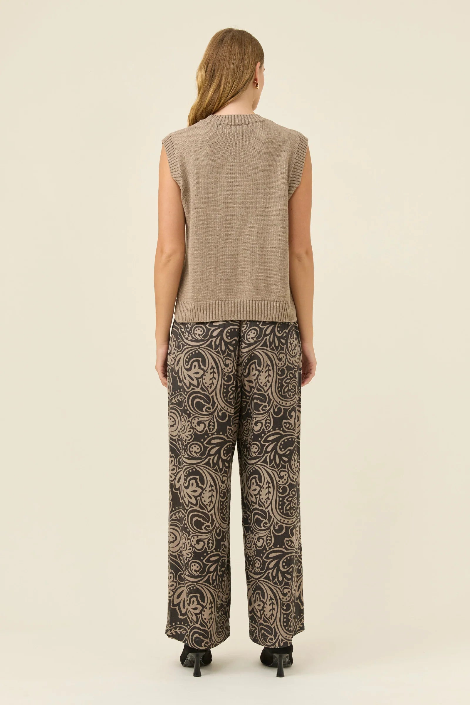 Image of Woman wearing a Isle of Mine beige sleeveless top and patterned pants on a white background
