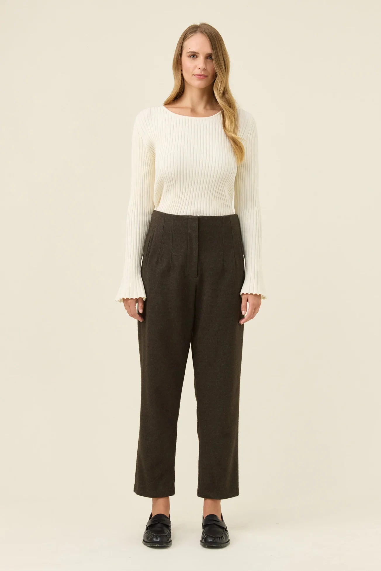 Image of Woman wearing a white sweater and Isle of Mine dark pants on a beige background