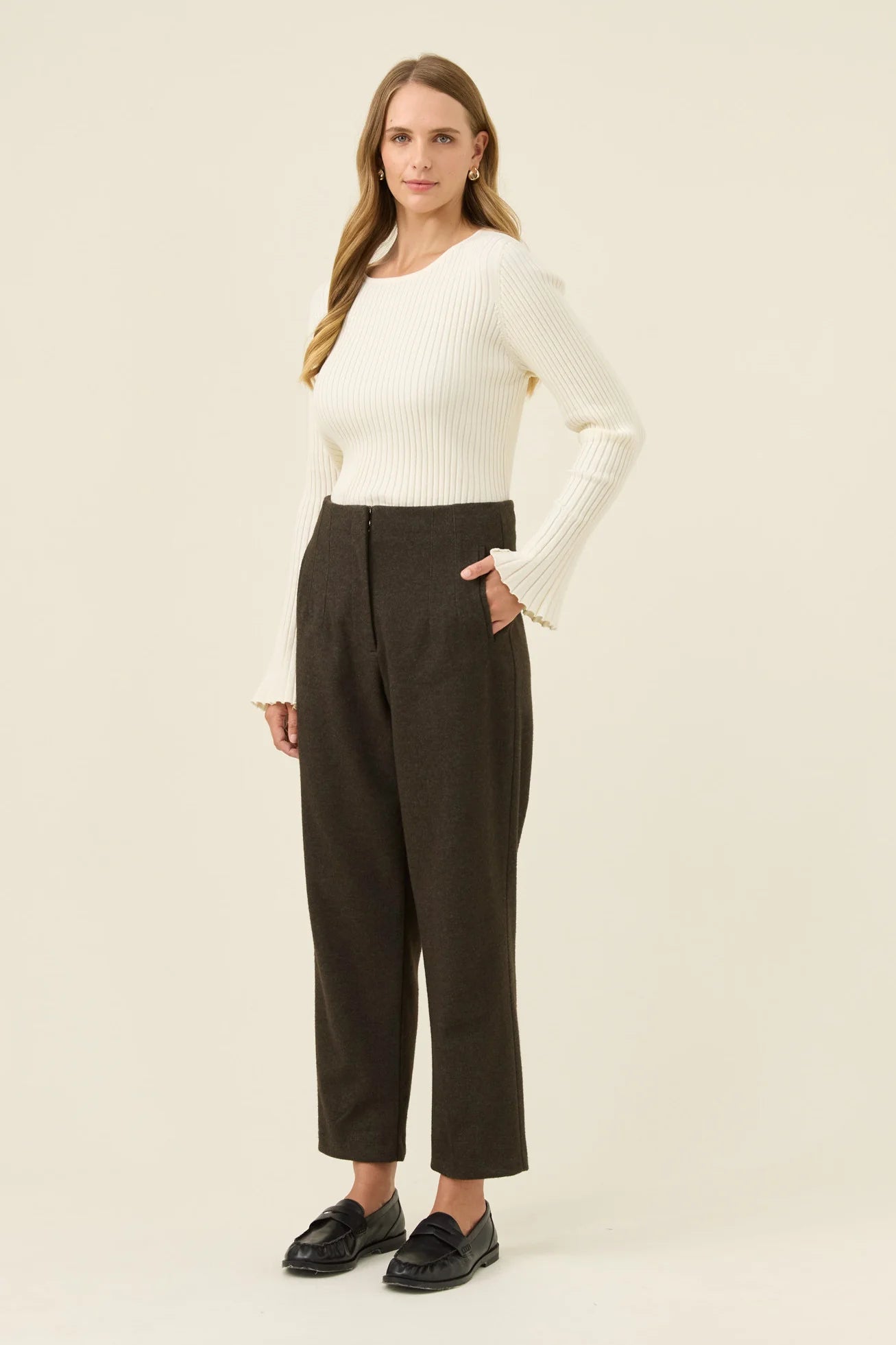 Image of Woman wearing a white sweater and Isle of Mine dark pants on a beige background