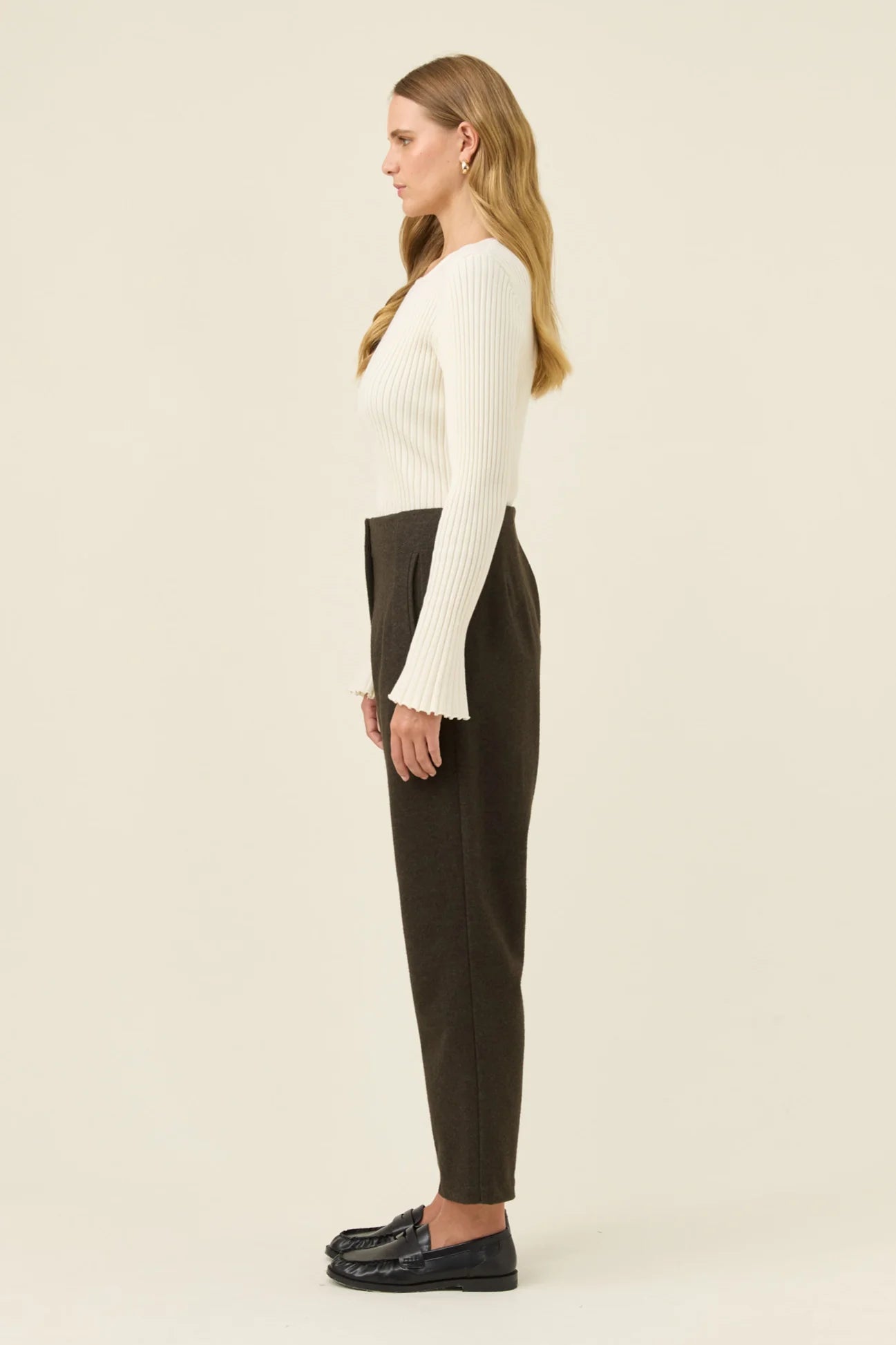 Image of Woman wearing a white long-sleeve top and Isle of Mine dark pants on a beige background