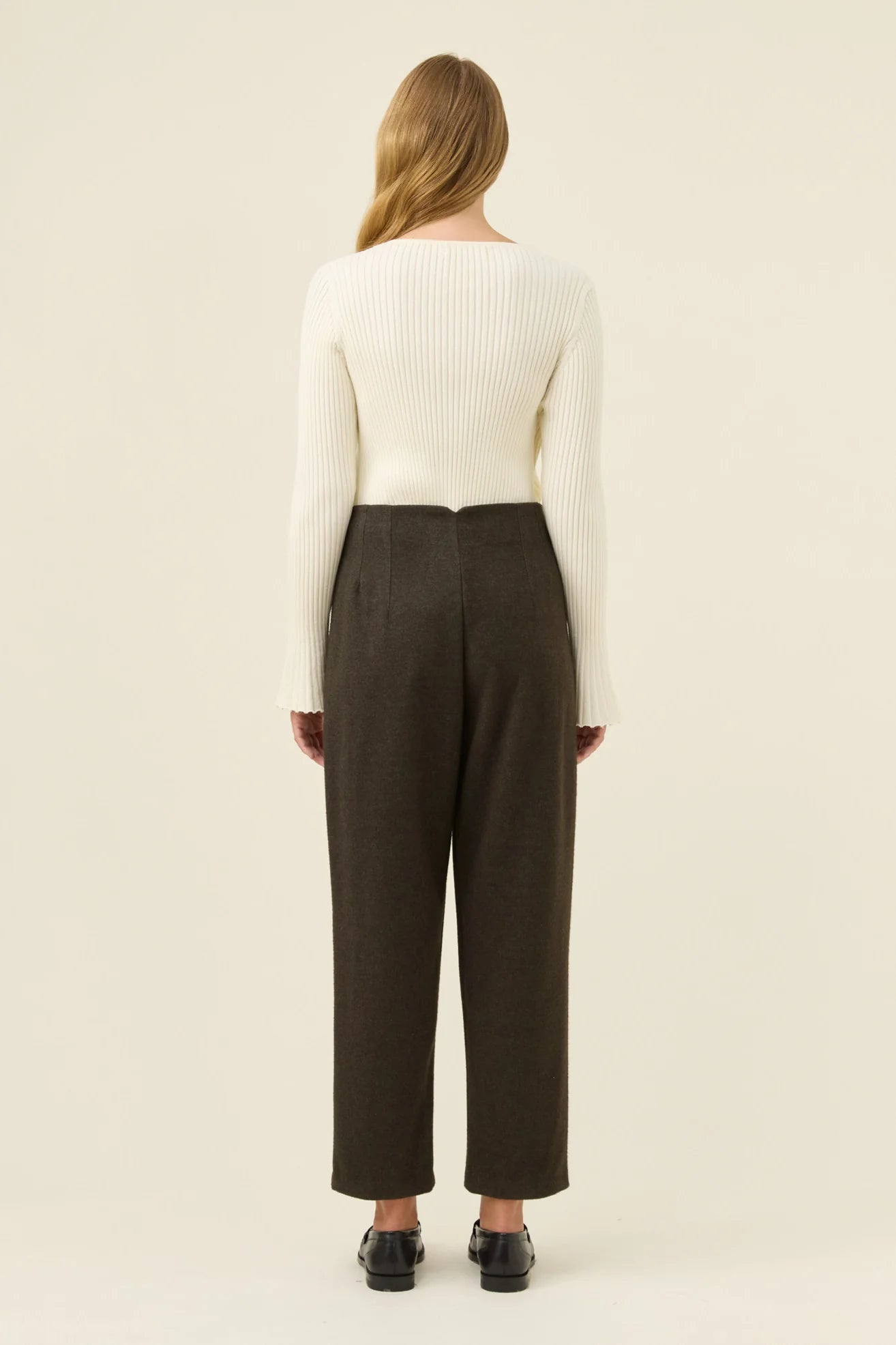 Woman wearing a white sweater and Isle of Mine brown pants on a beige background