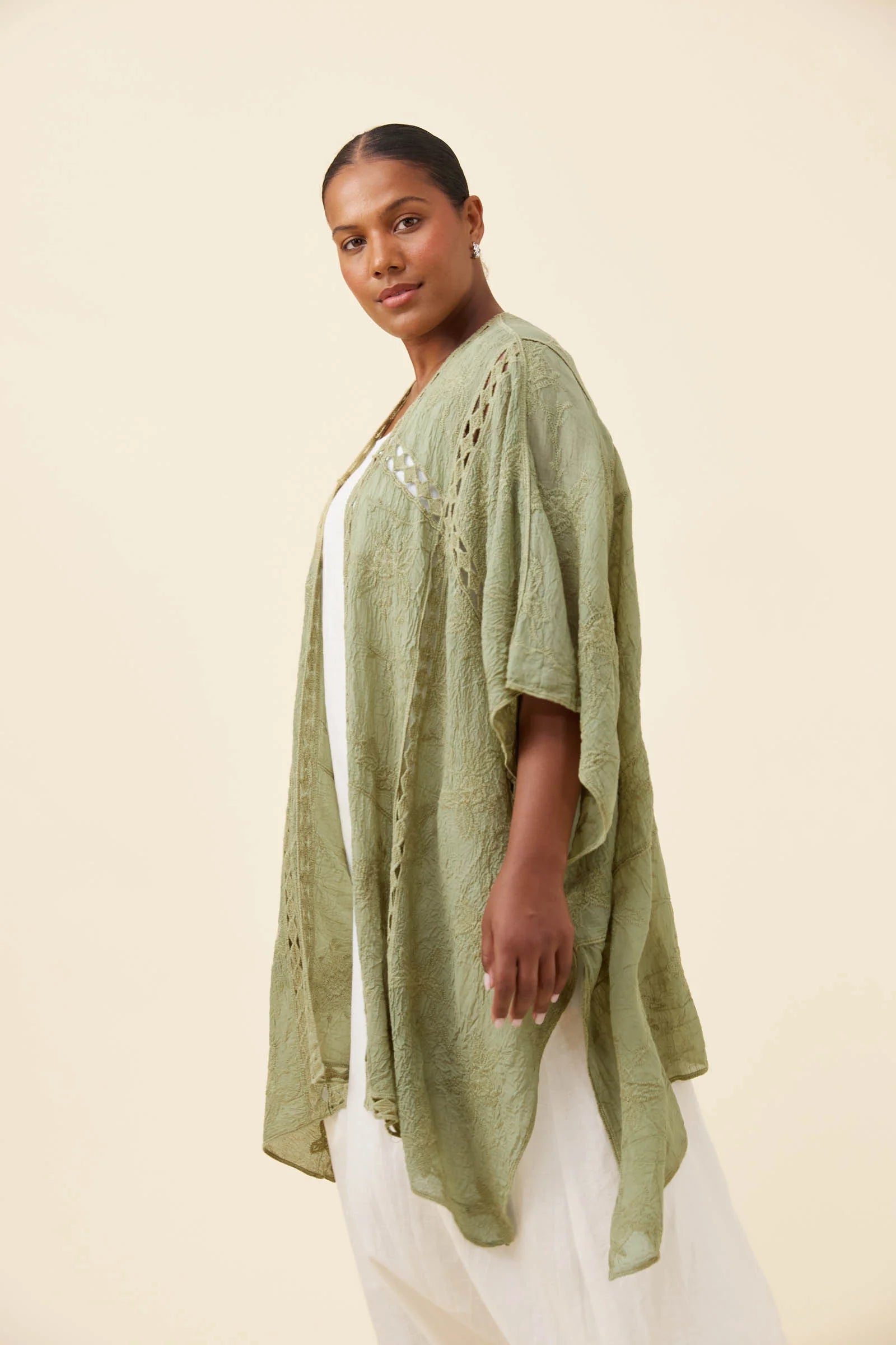 Image of A woman modeling a Isle of Mine light sage green textured open-front cardigan with crochet details over a white top and white pants, set against a solid cream background.