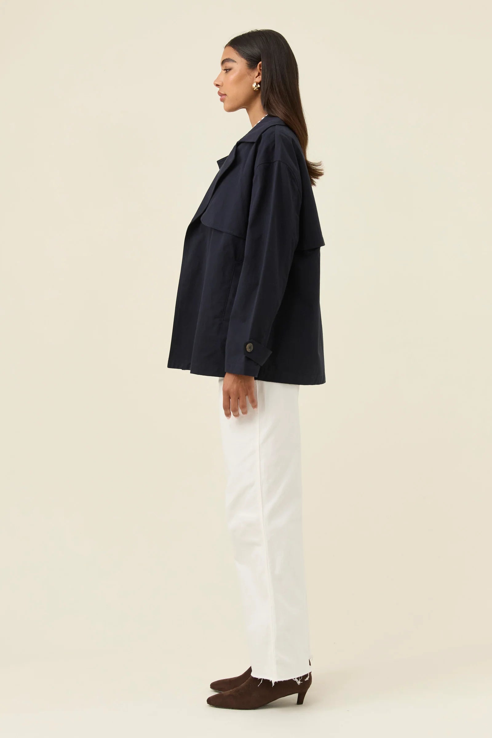 Woman wearing a Isle of Mine navy jacket and white pants on a beige background