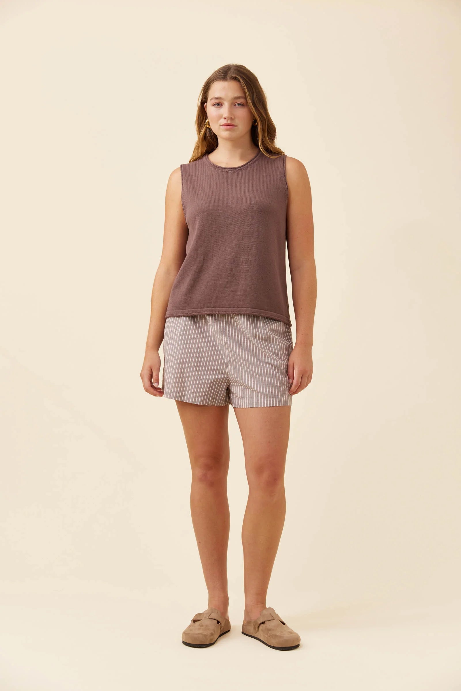 Image of A woman modeling a Isle of Mine sleeveless dusty mauve top and light beige and white striped shorts against a solid cream background.
