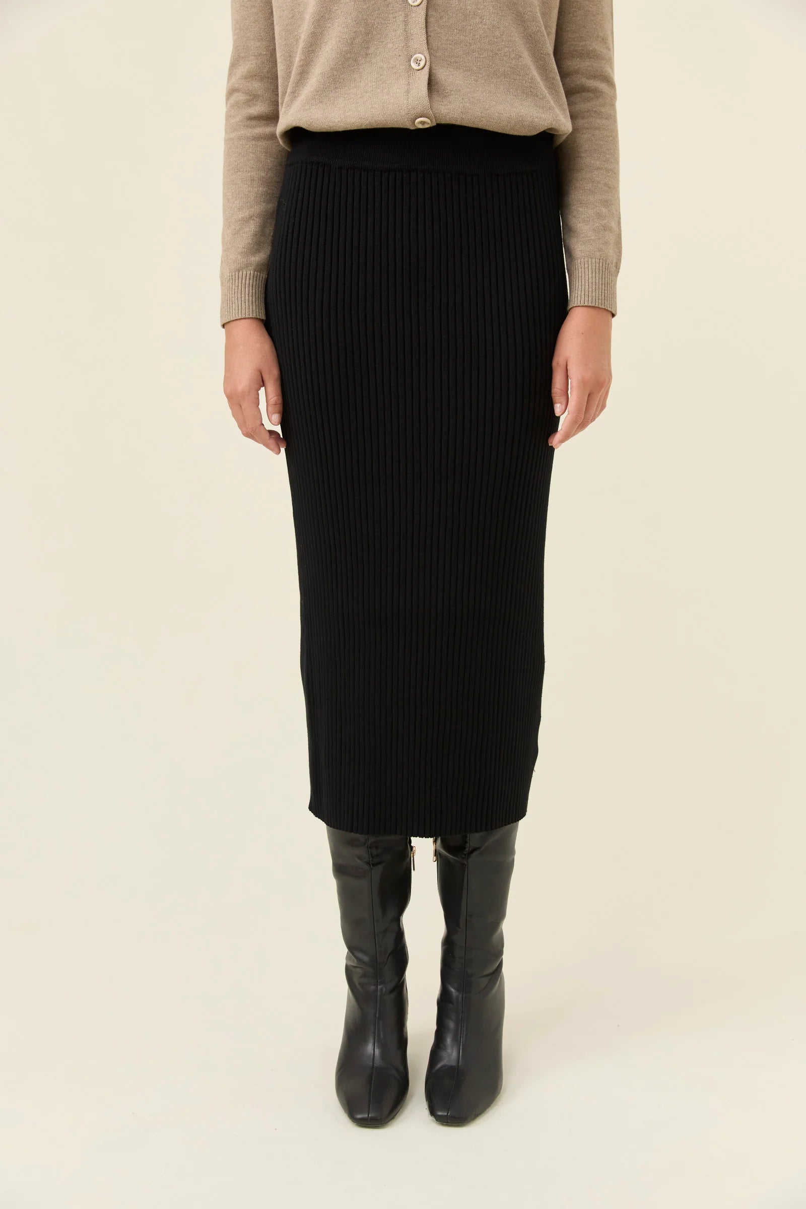 Image of Woman wearing Isle of Mine black knit skirt paired with a beige jumper on a plain background 