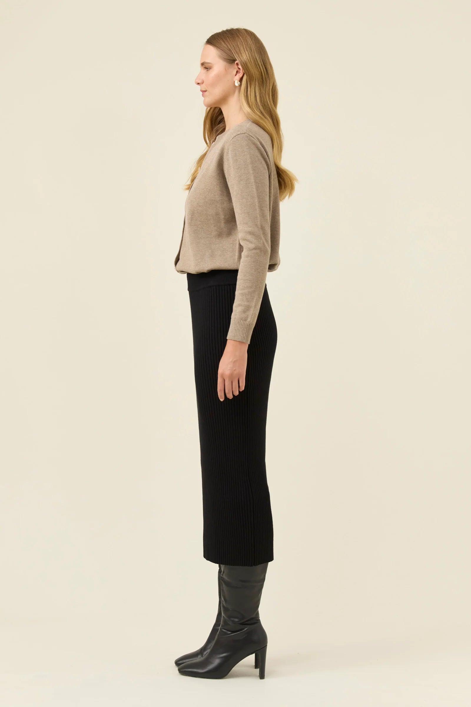 Image of Woman wearing Isle of Mine black knit skirt paired with a beige jumper on a plain background 