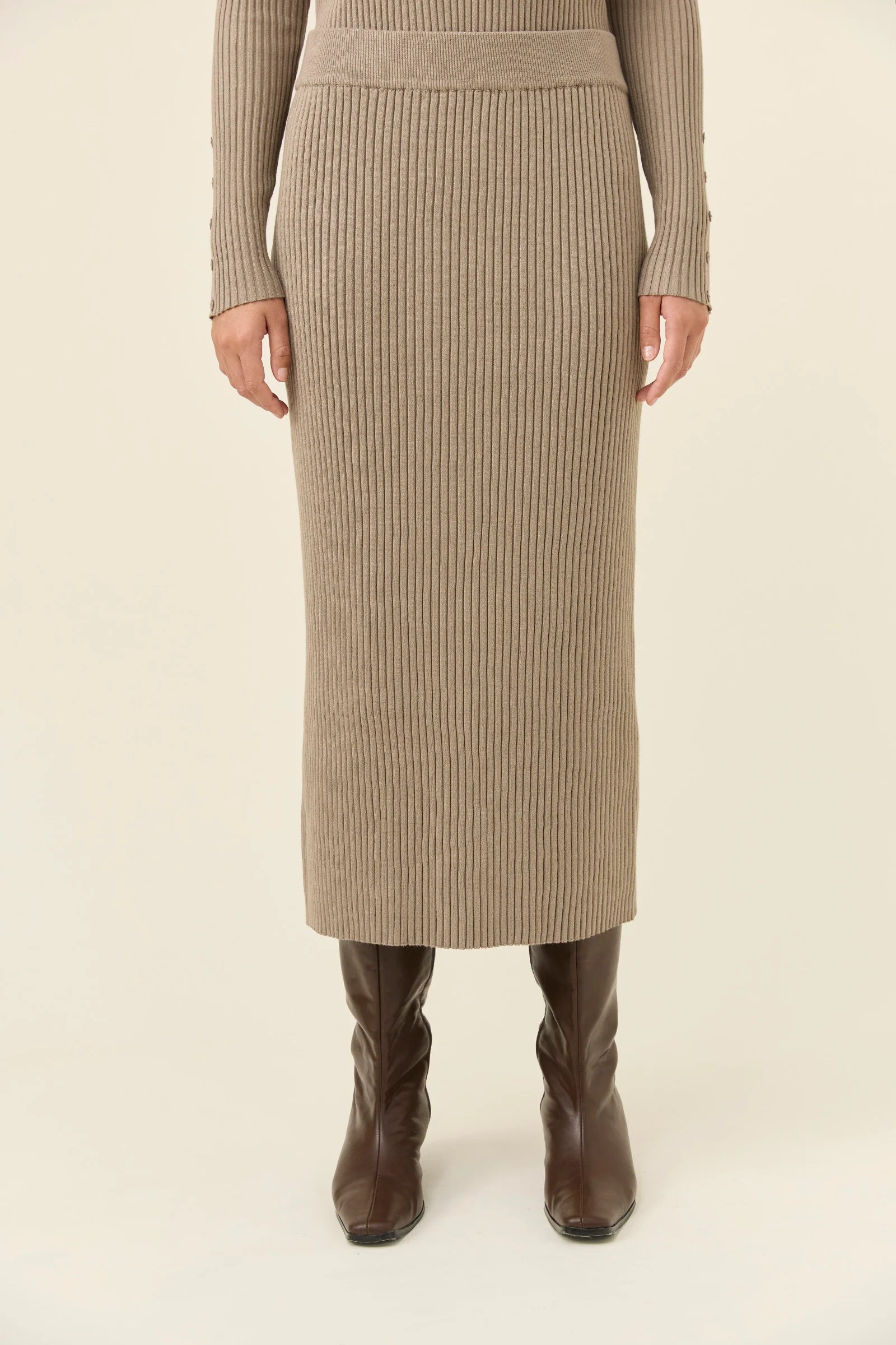 Image of Woman wearing a Isle of Mine beige ribbed skirt and brown boots on a white background