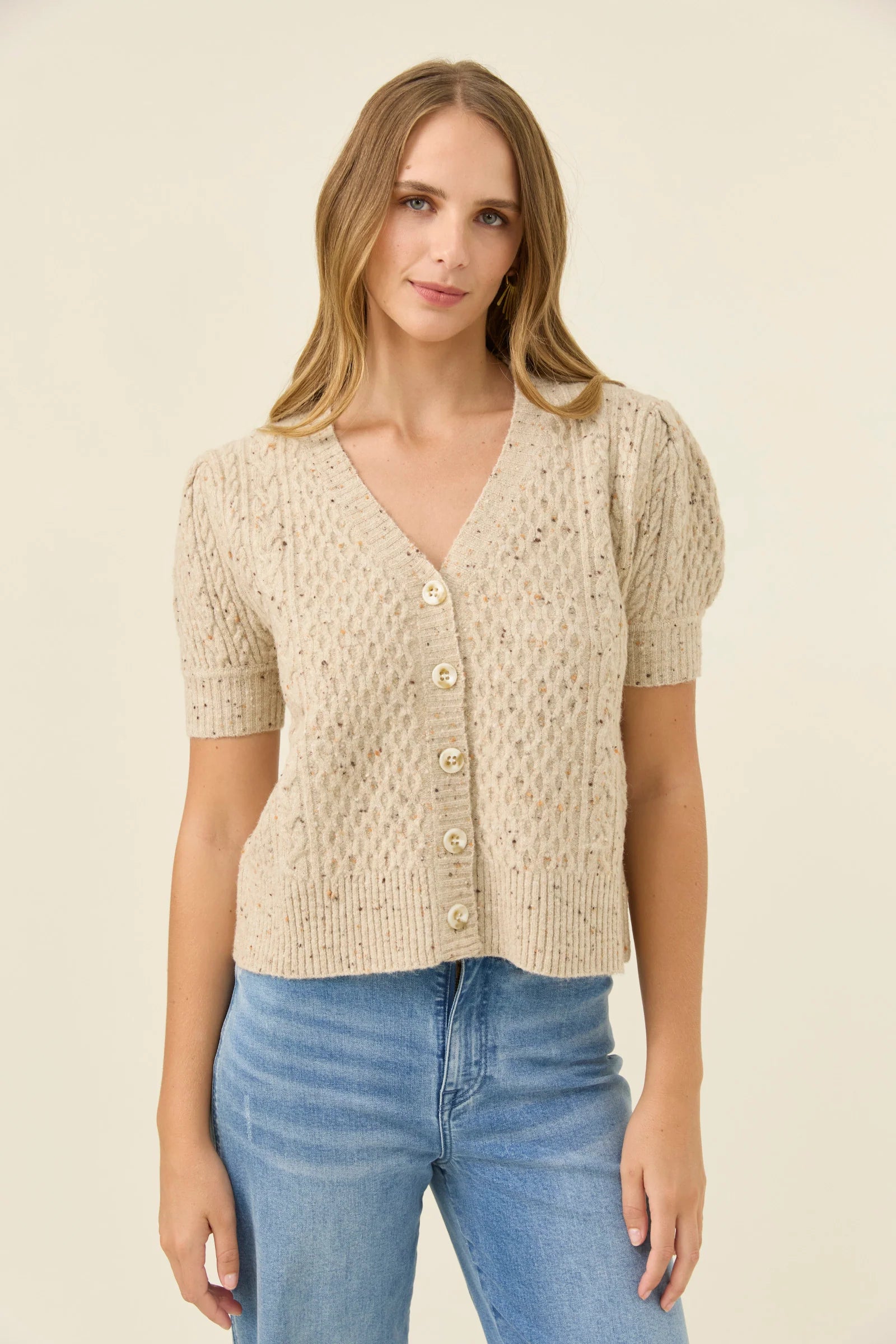 Image of Woman wearing a Isle of Mine beige knitted cardigan and blue jeans on a plain background