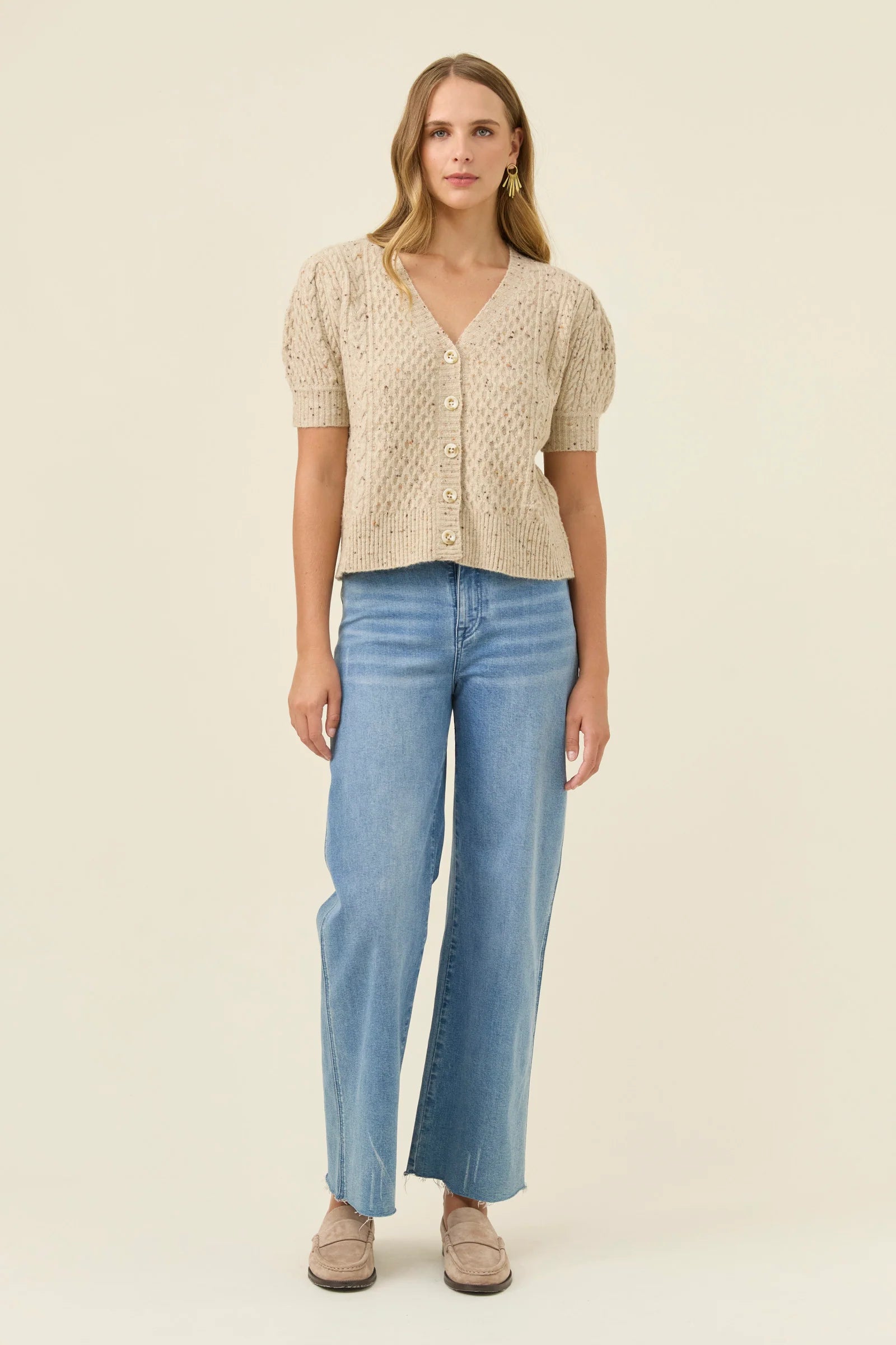 Woman wearing a Isle of Mine beige knitted top and blue jeans on a beige background