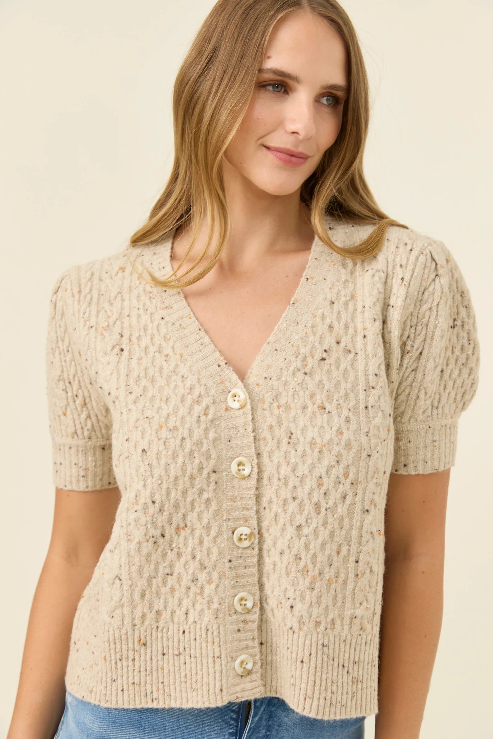 Woman wearing a Isle of Mine beige knitted cardigan with buttons on a plain background
