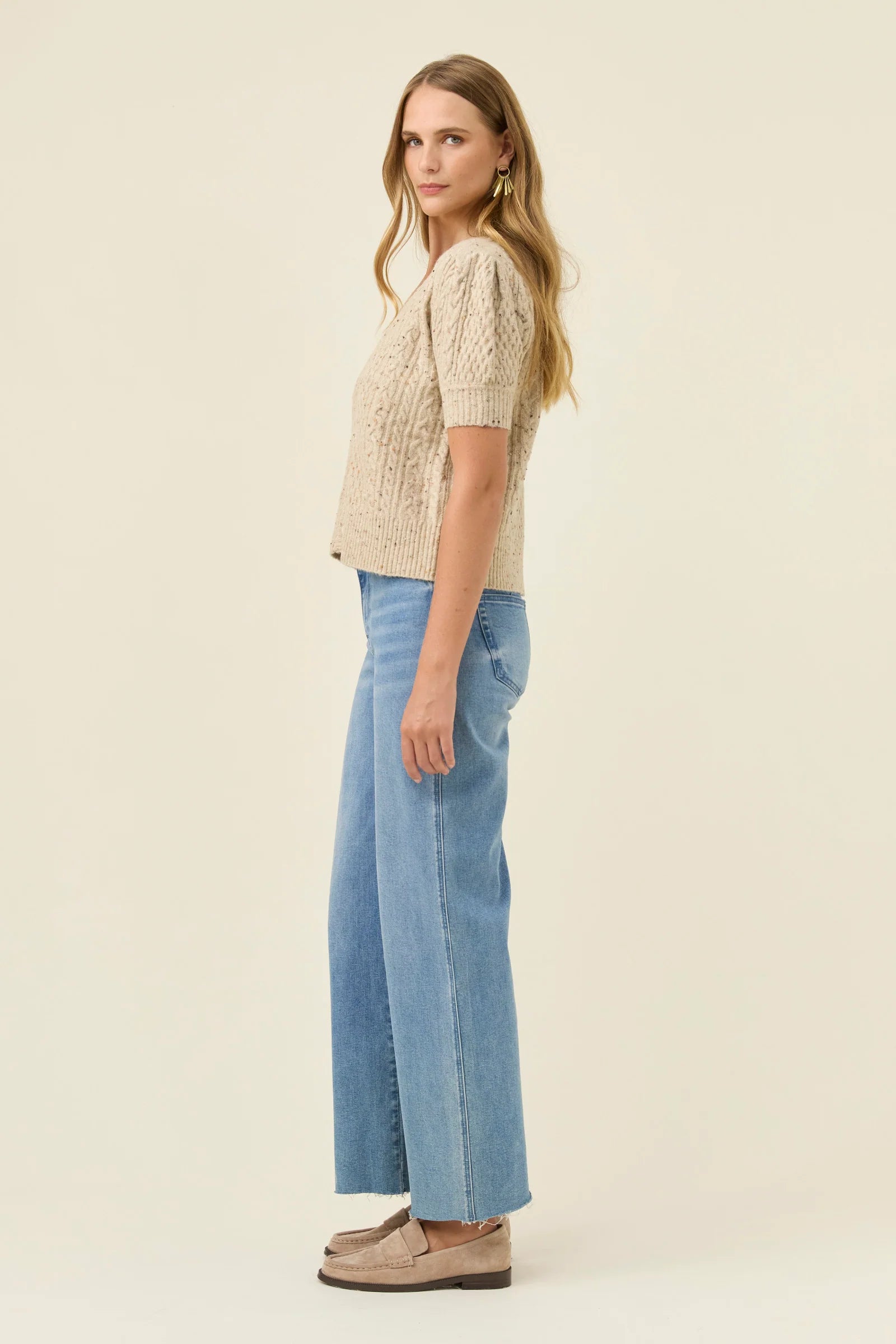 Woman wearing a Isle of Mine beige knitted top and blue jeans on a beige background