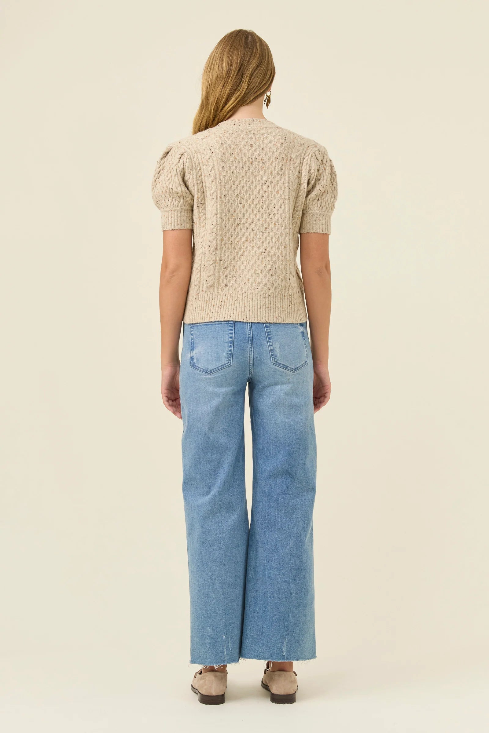 Woman wearing a Isle of Mine beige knitted sweater and light blue jeans on a beige background