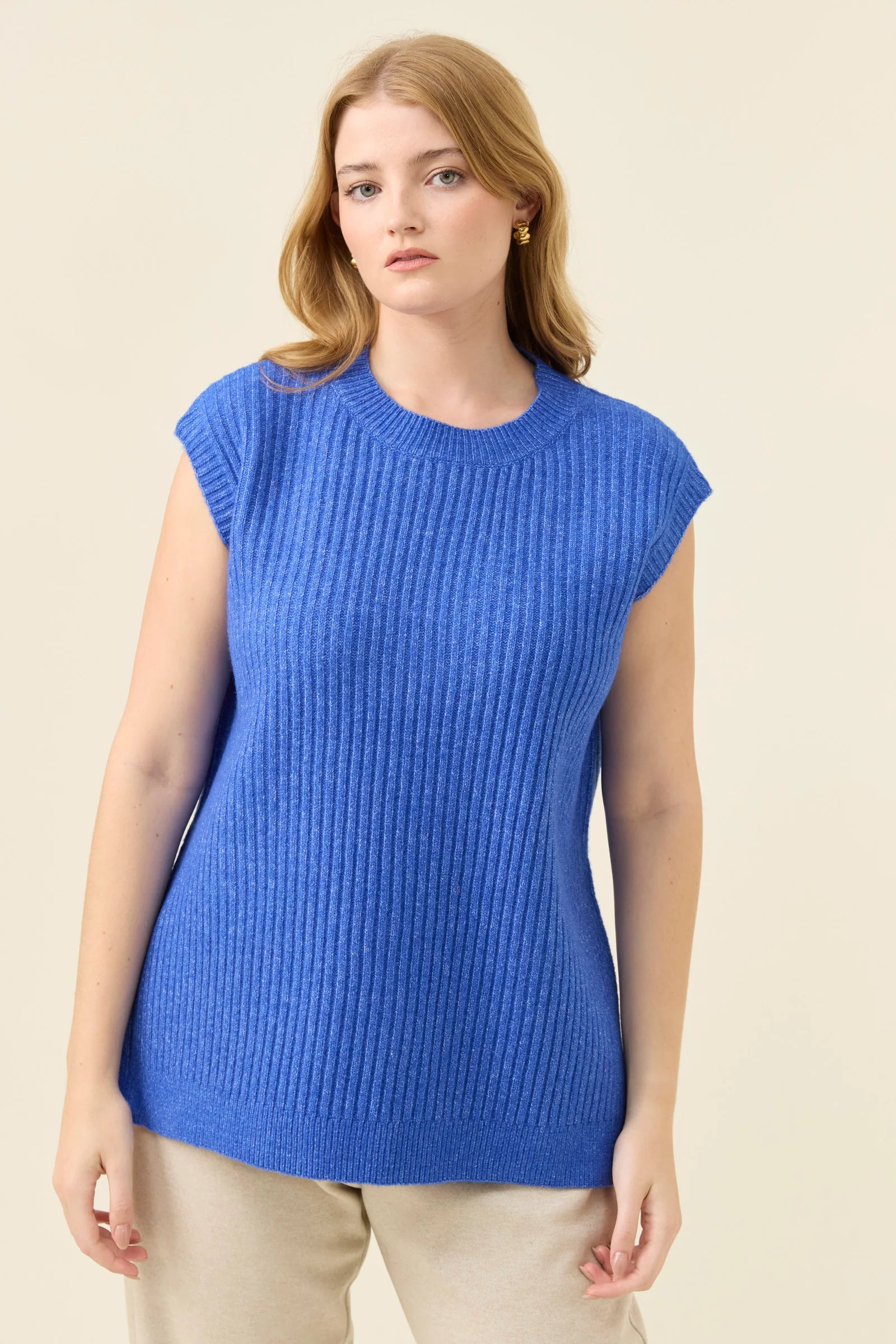 Woman wearing a Isle of Mine blue sleeveless sweater against a beige background