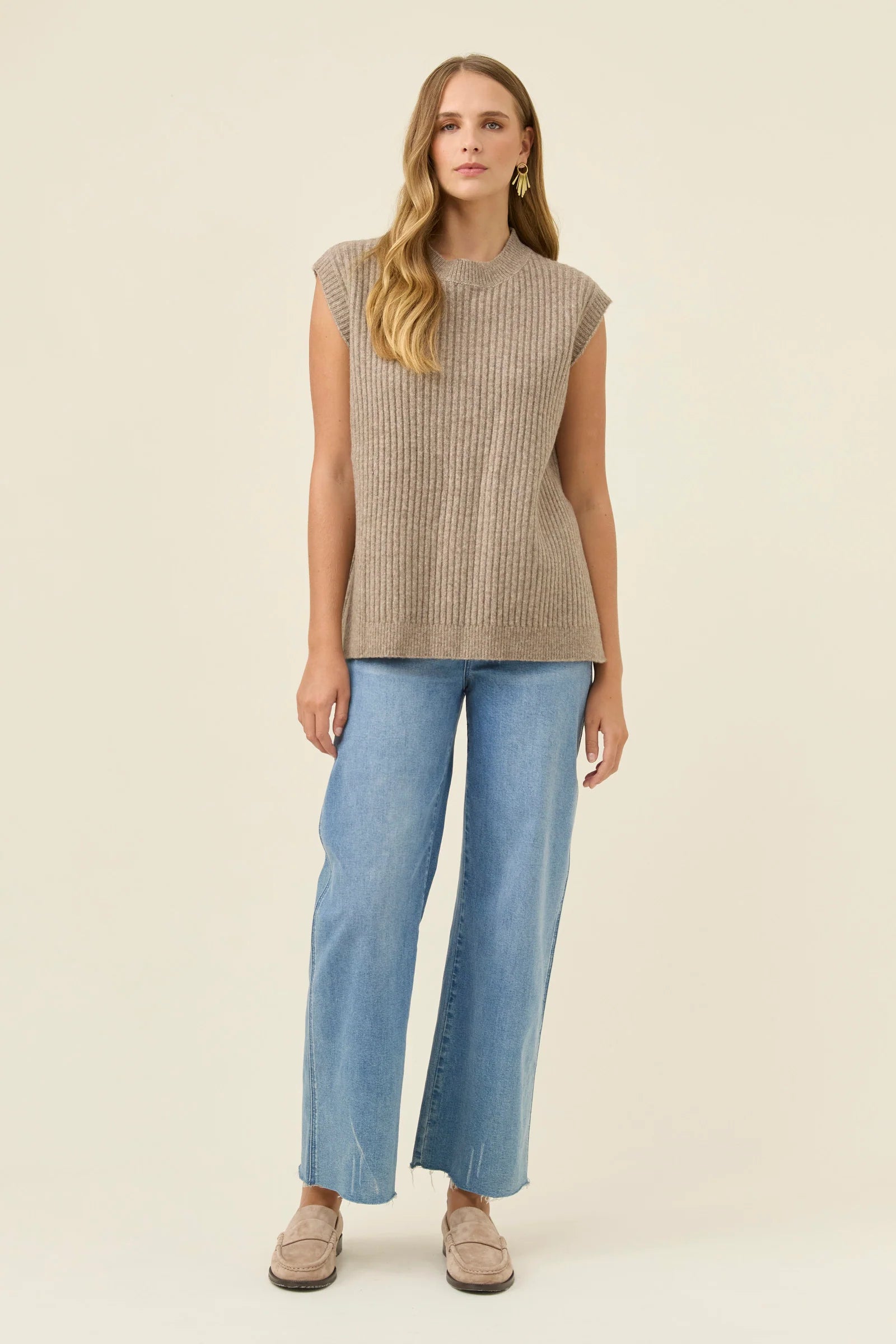 Woman wearing an Isle of Mine beige vest with denim jeans on a white coloured background