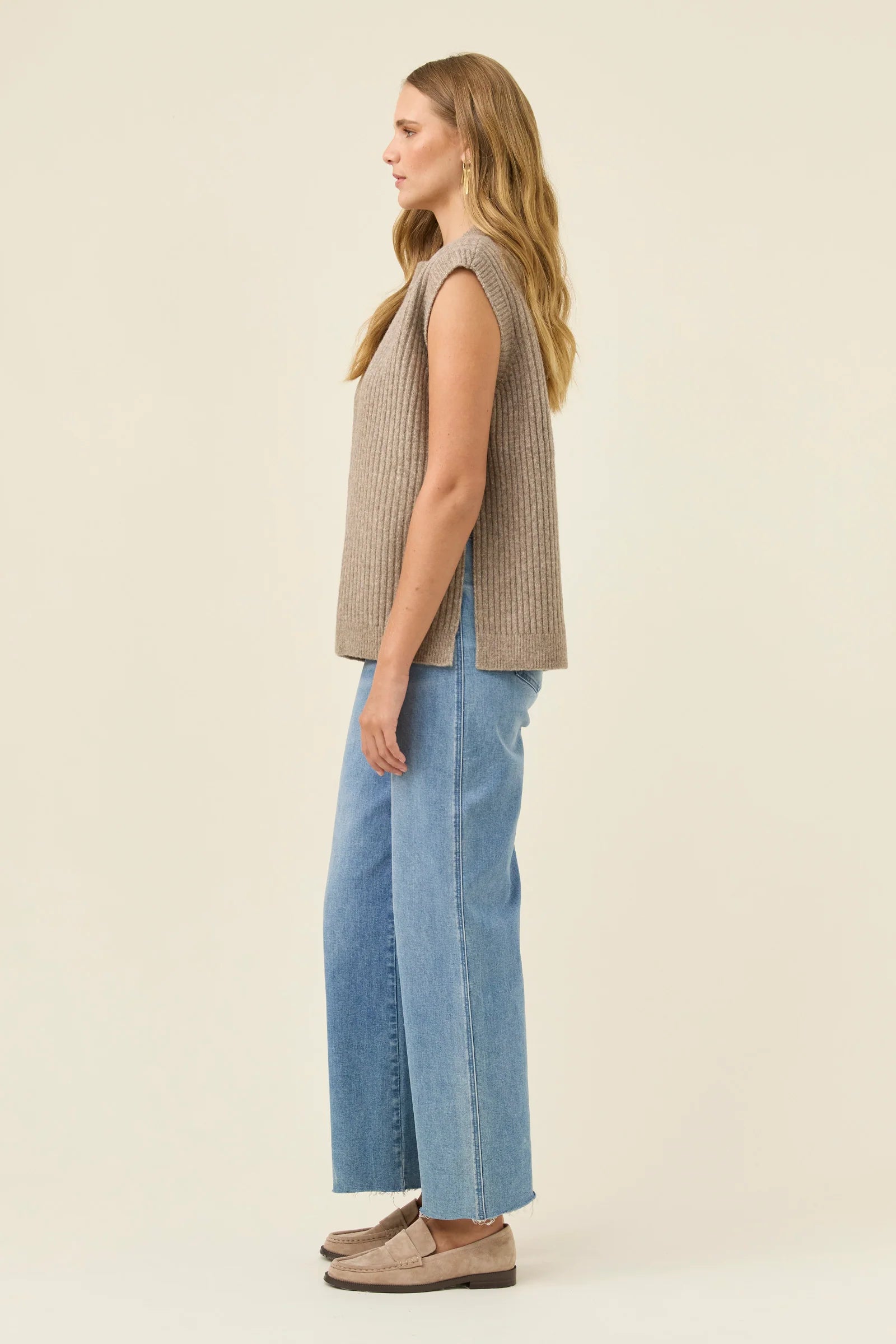 Image of Woman wearing a Isle of Mine sleeveless brown knit top and light blue jeans on a beige background