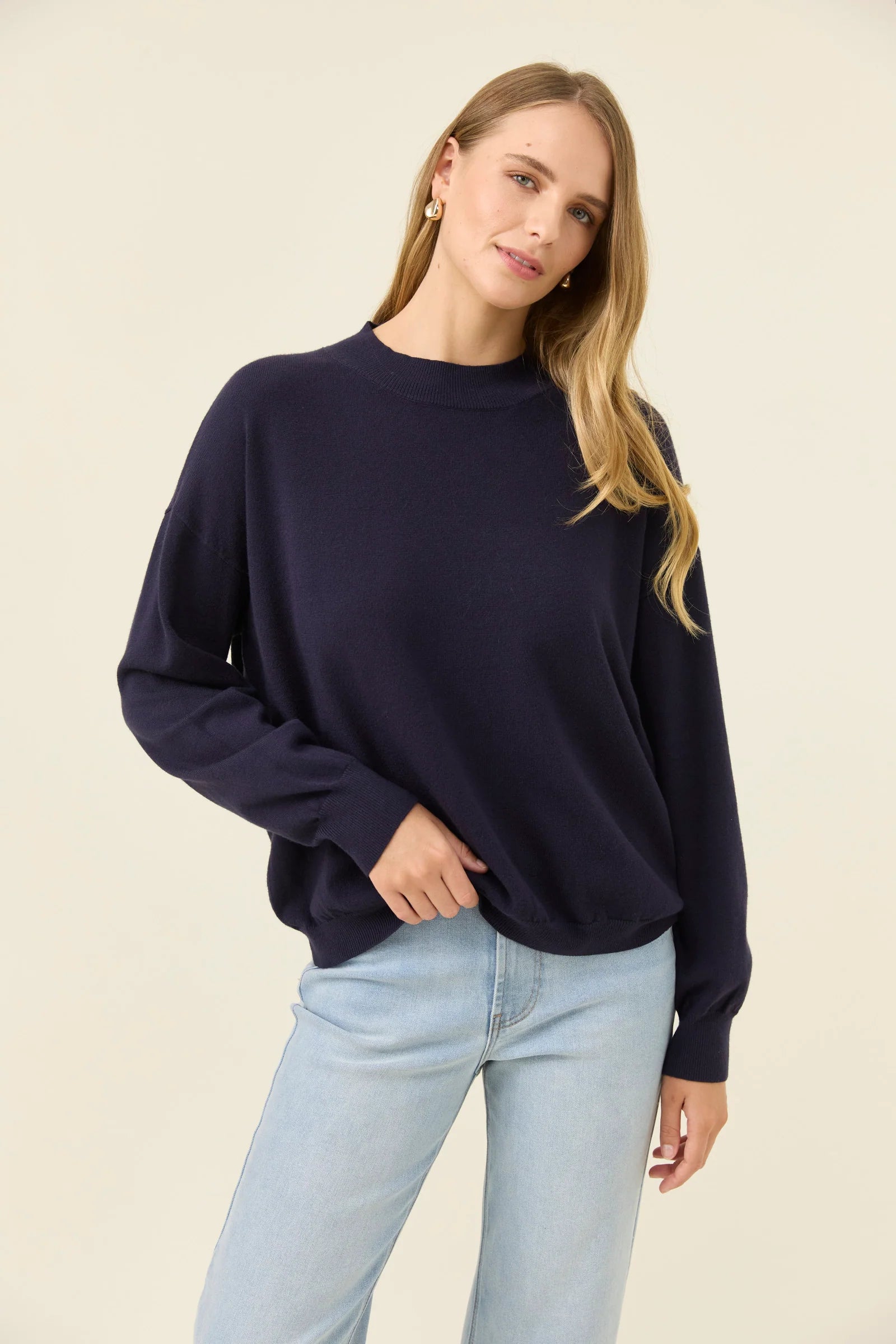 Image of Woman wearing a Isle of Mine navy sweater and light blue jeans on a beige background