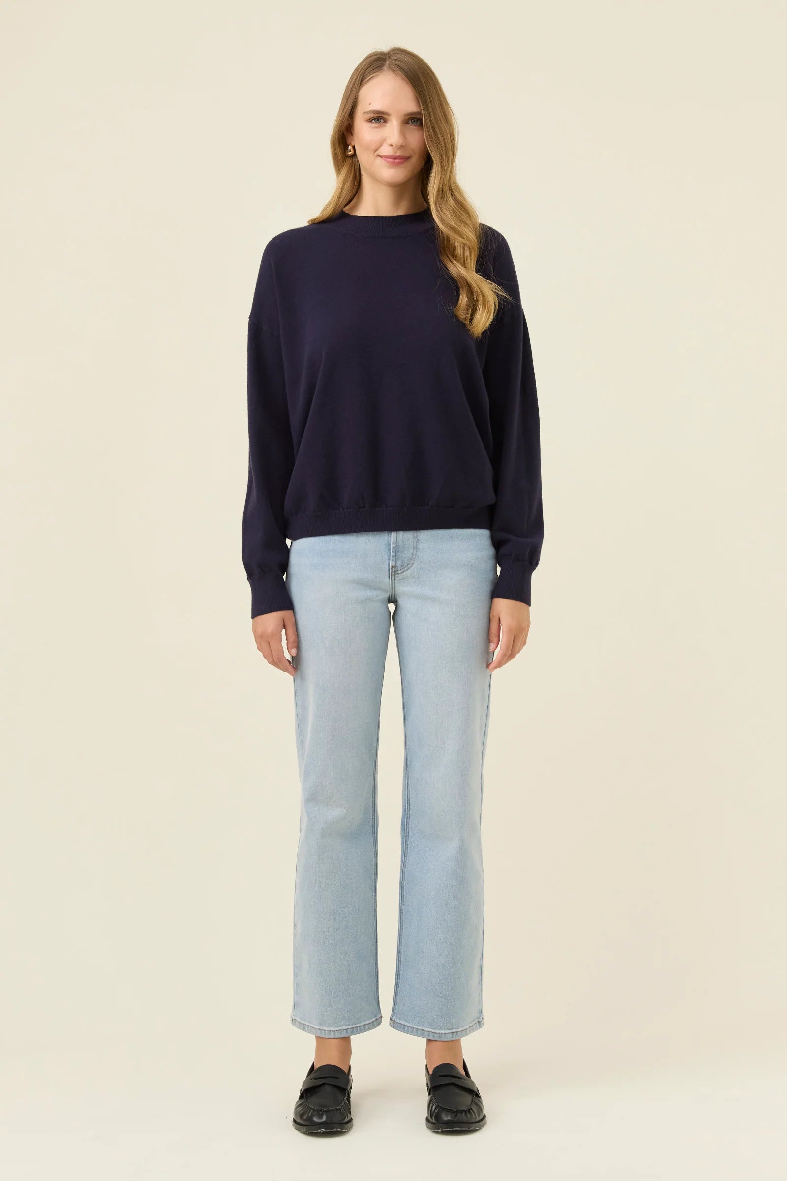 Image of Woman wearing a Isle of Mine navy sweater and light blue jeans on a beige background