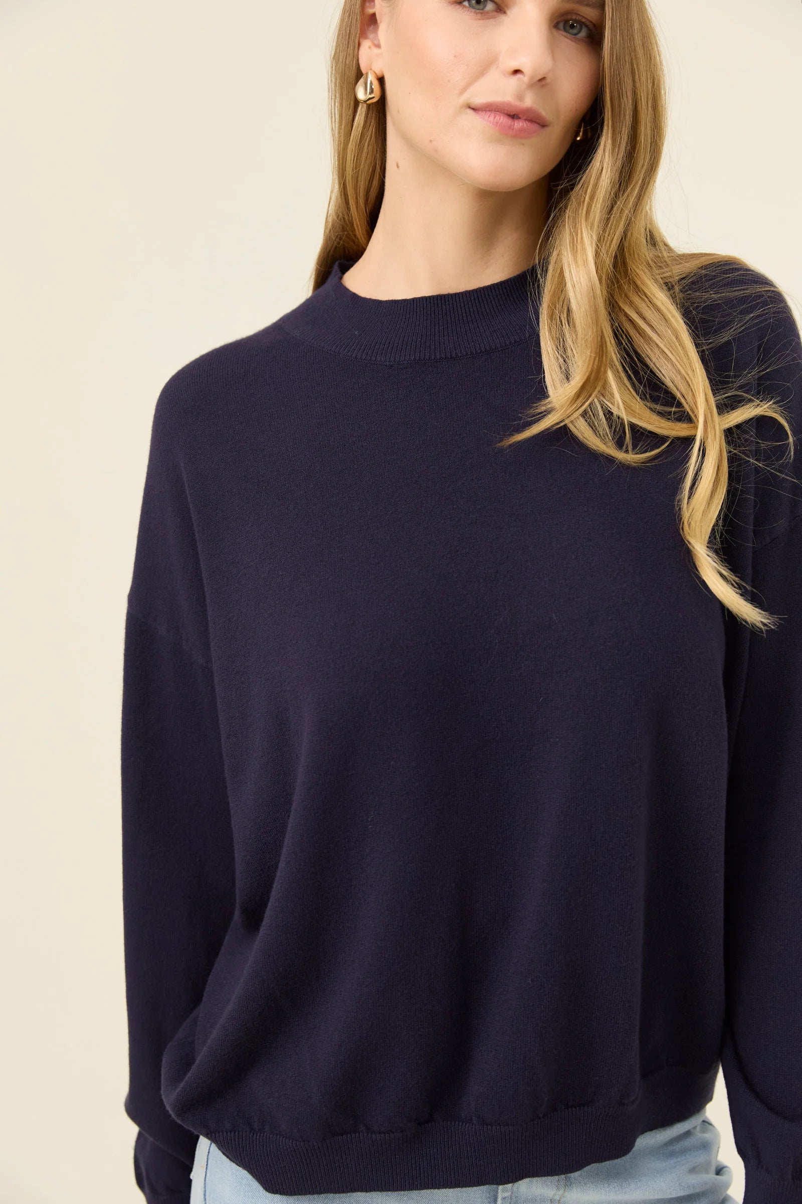 Woman wearing a Isle of Mine navy blue sweater against a beige background