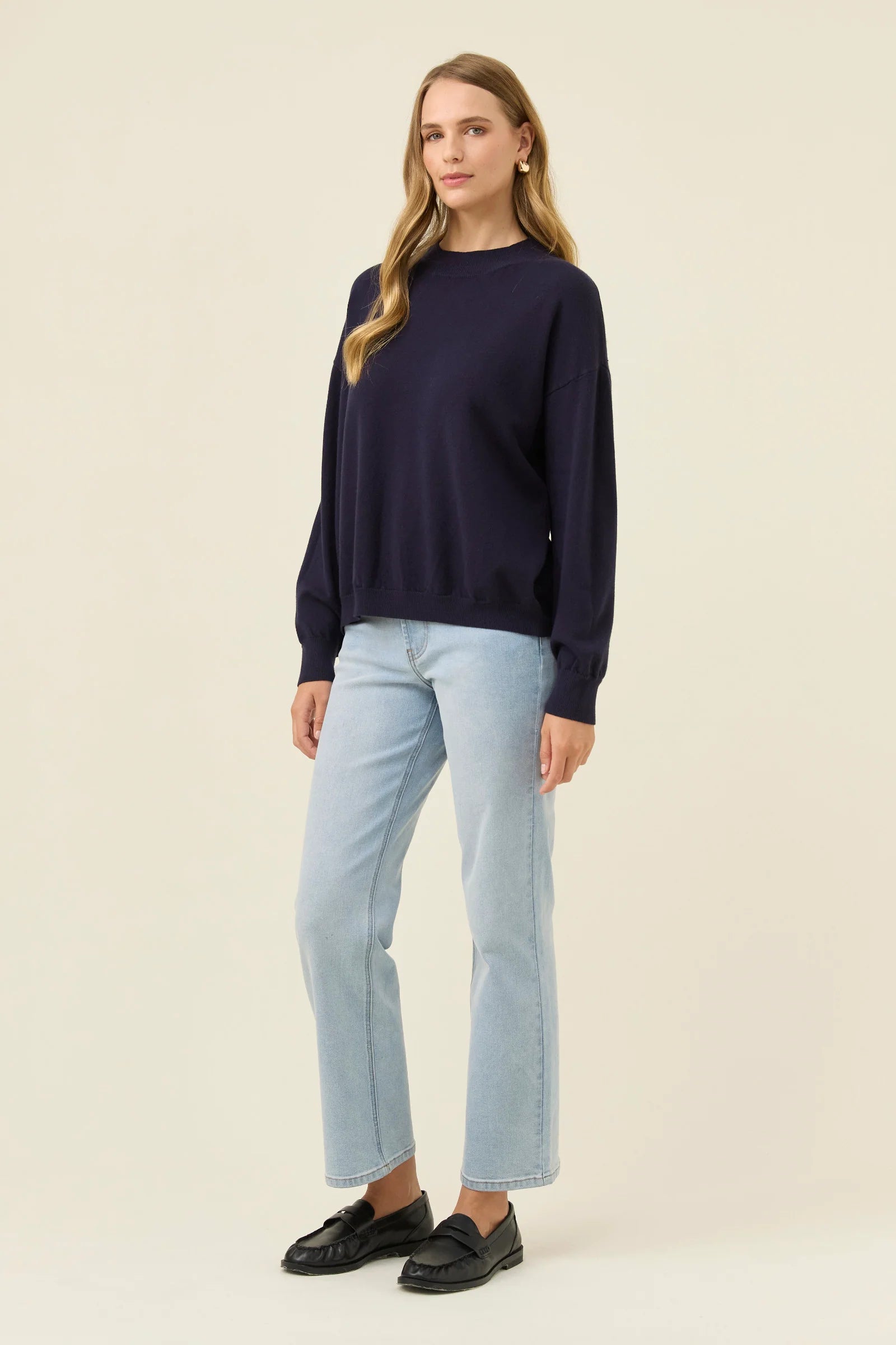 Woman wearing a Isle of Mine navy sweater and light blue jeans on a beige background