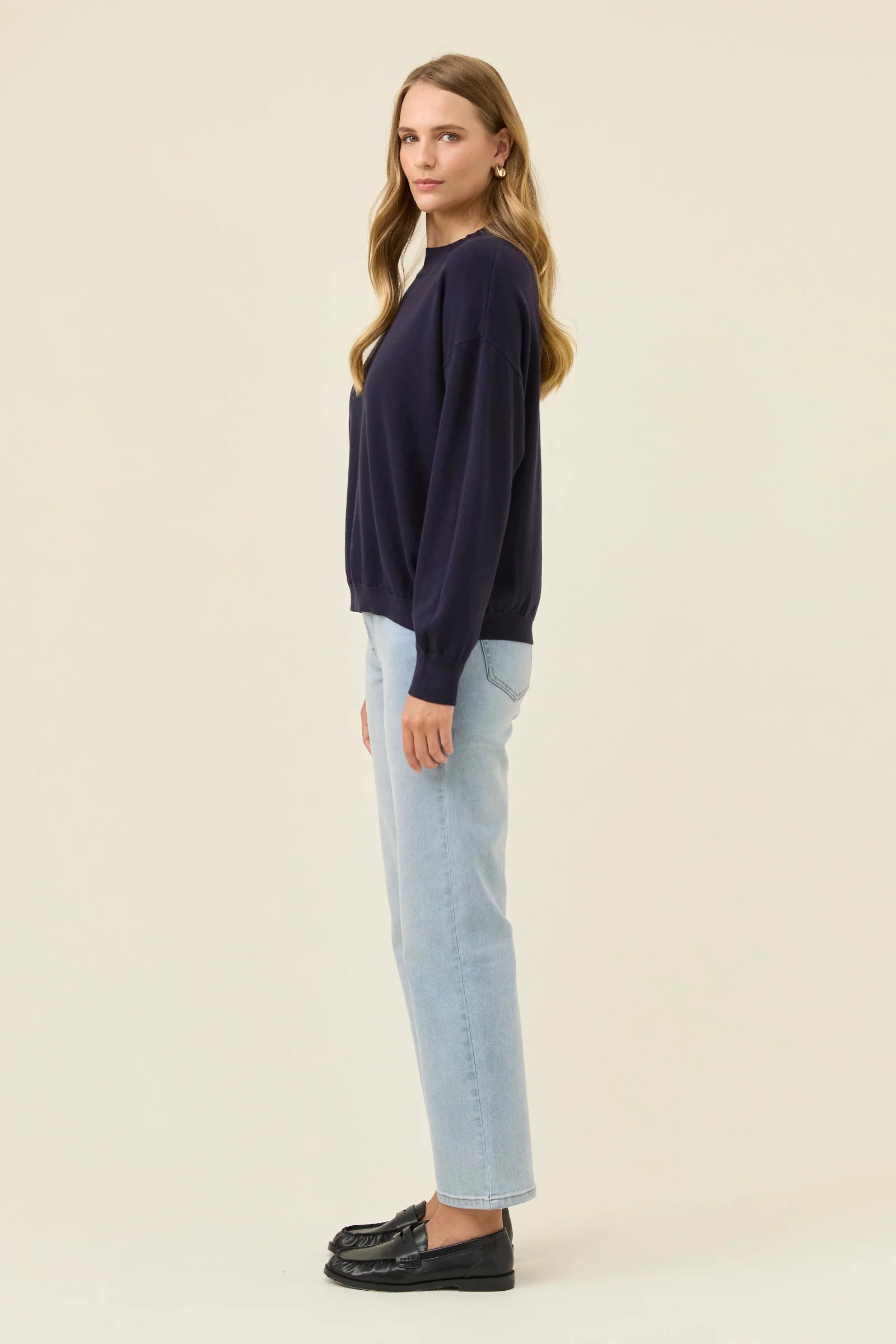 Image of Woman wearing a Isle of Mine navy sweater and light blue jeans on a beige background