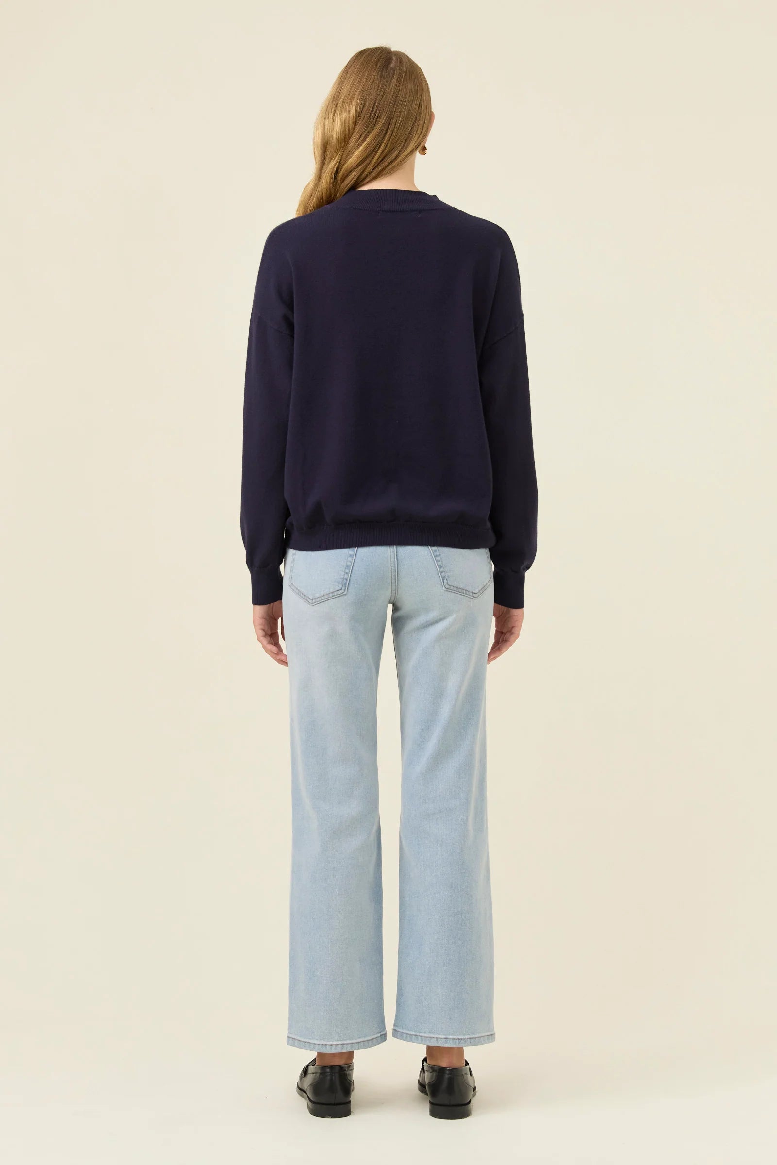 Image of Woman wearing a Isle of Mine navy sweater and light blue jeans on a beige background