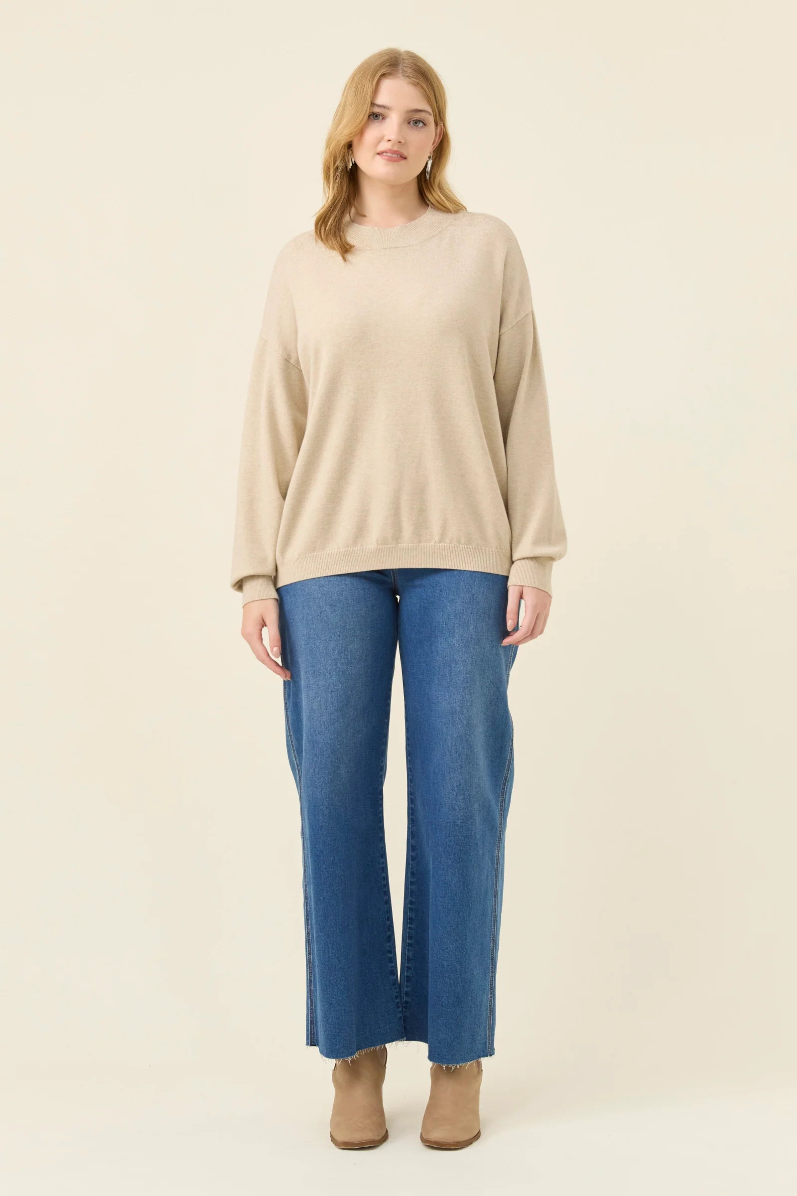 Woman wearing a Isle of Mine beige sweater and blue jeans on a white background