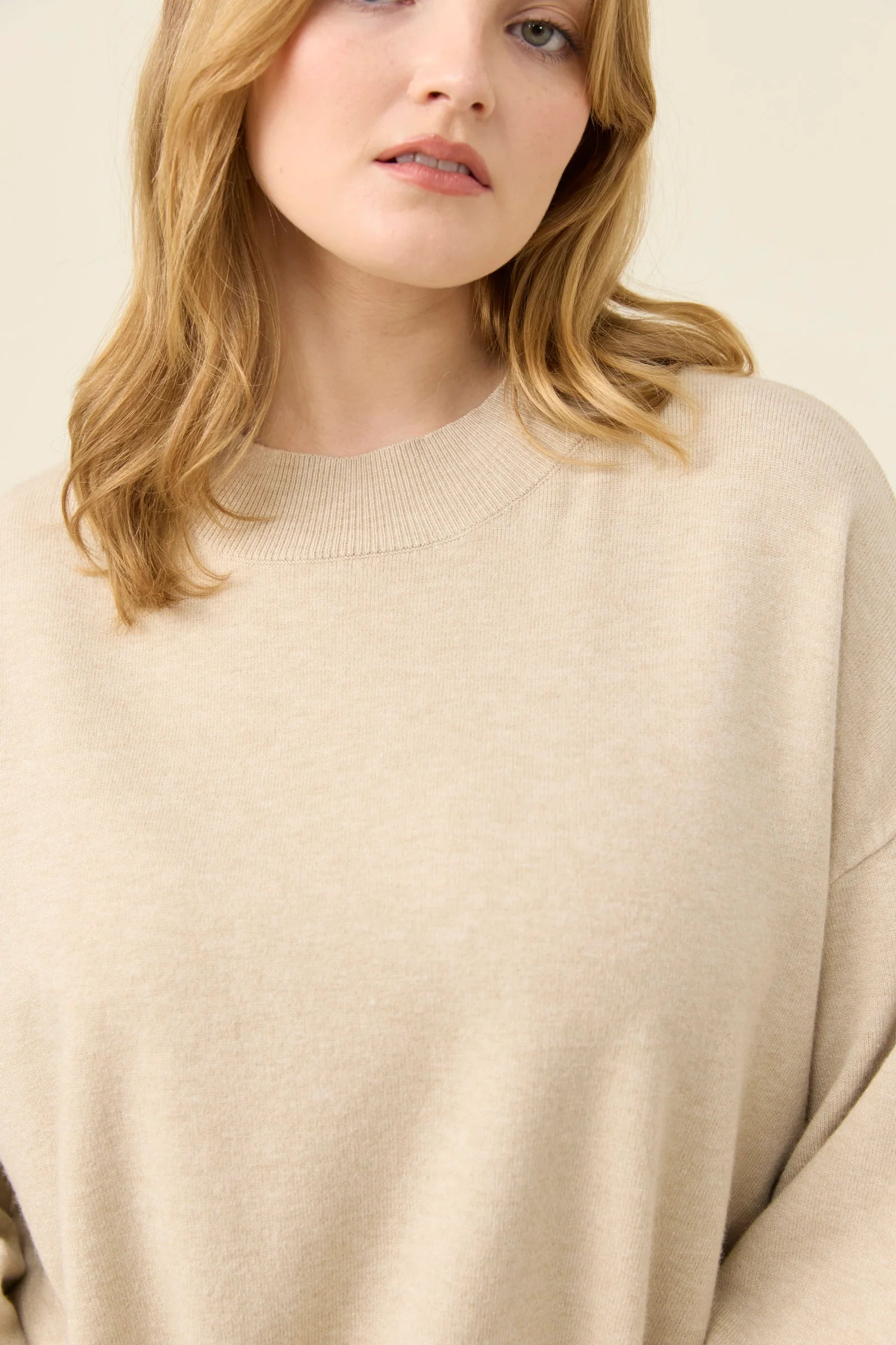 Woman wearing a Isle of Mine beige sweater and blue jeans on a white background
