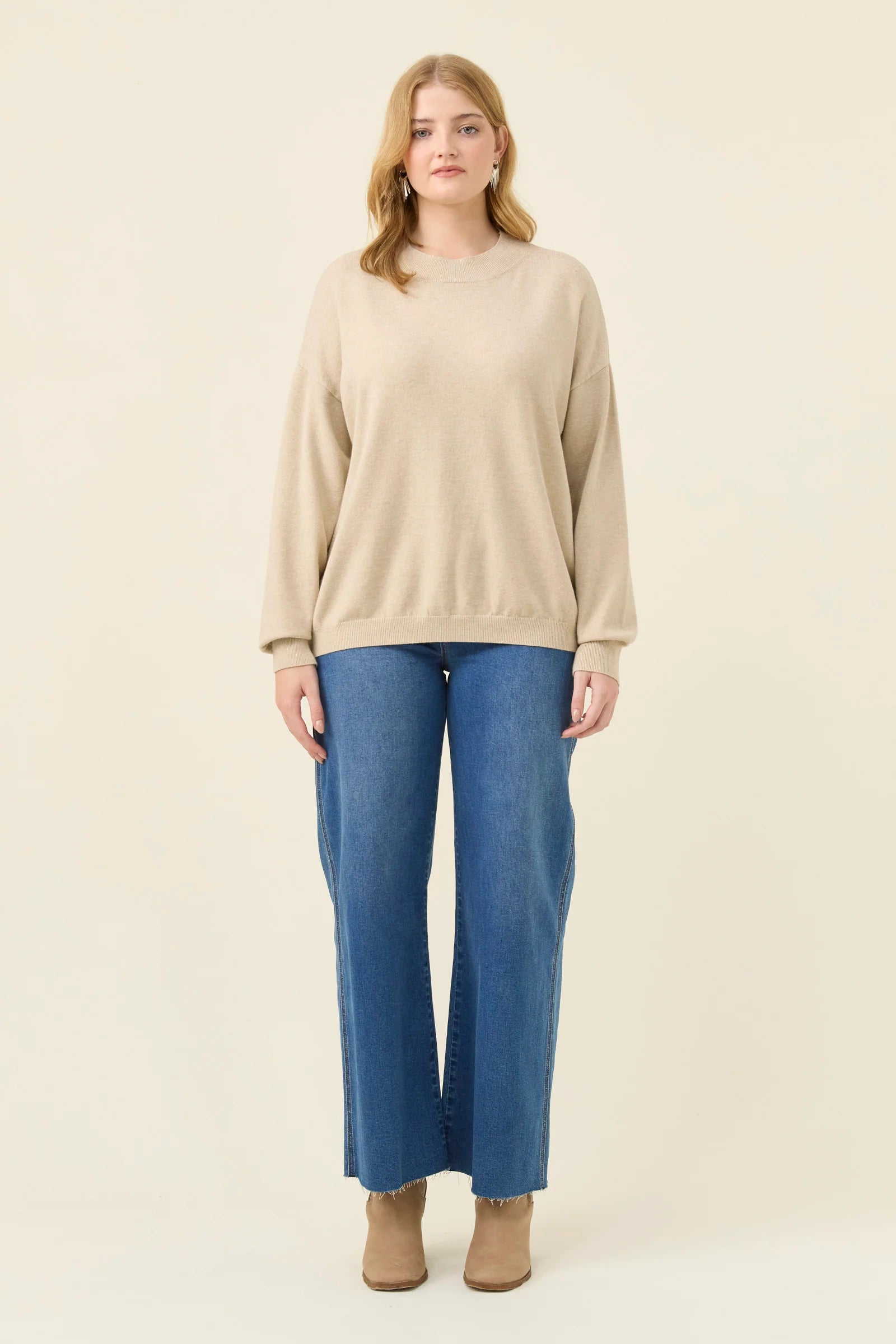 Woman wearing a Isle of Mine beige sweater and blue jeans on a white background