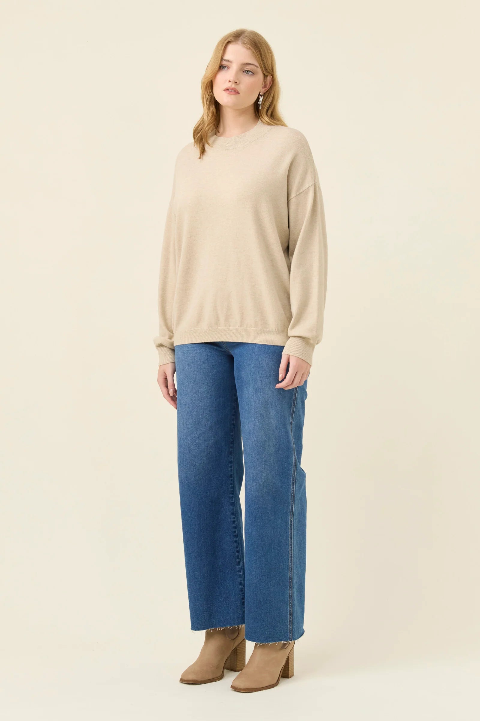 Woman wearing a Isle of Mine beige sweater and blue jeans on a white background